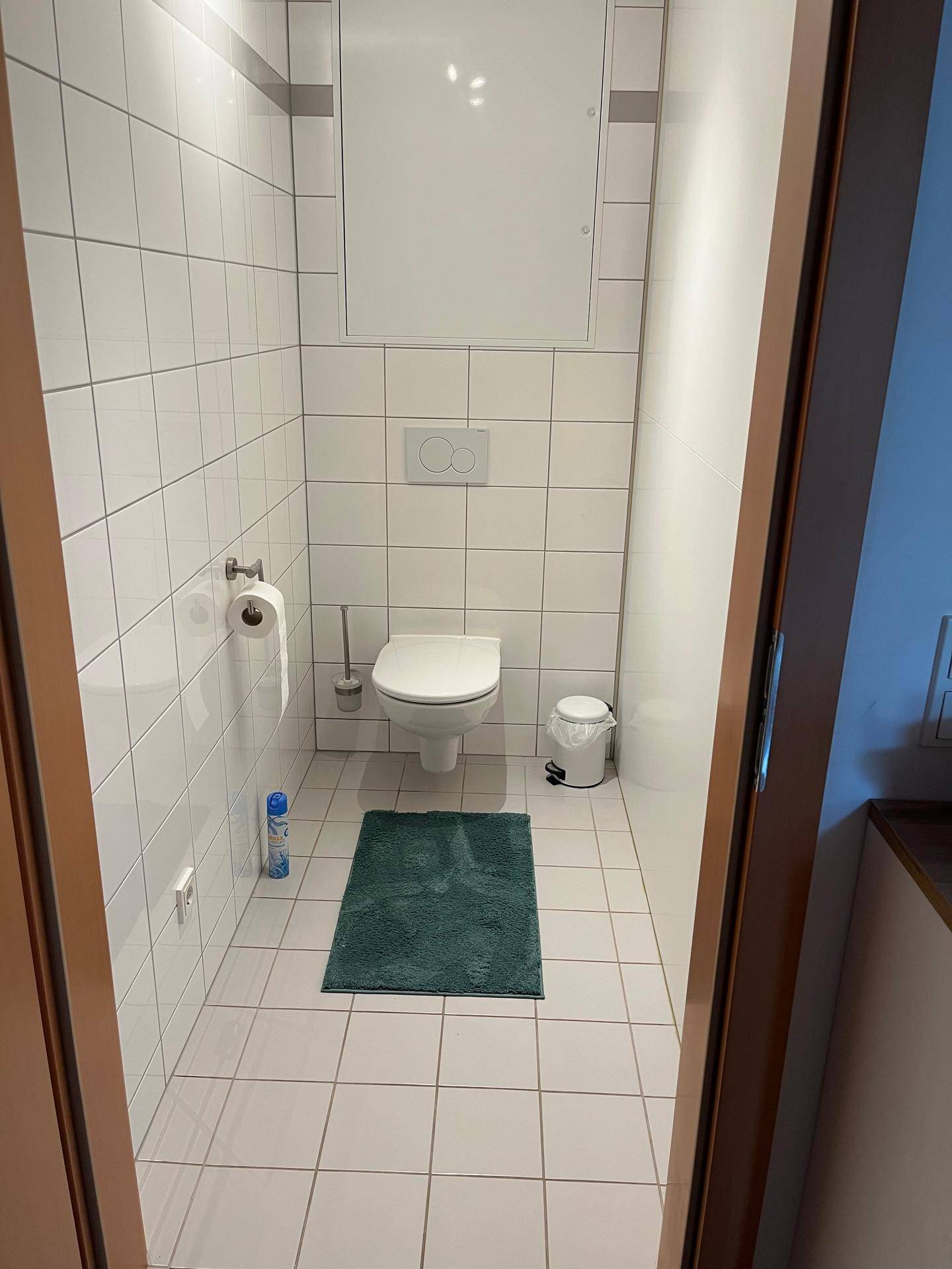 Kleines, gefliestes Gäste-WC mit wandhängender Toilette und weißem Fliesenboden.