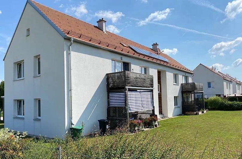 Seitenansicht eines Wohnhauses mit Ziegeldach, Solaranlage und Balkonen in ländlicher Umgebung.