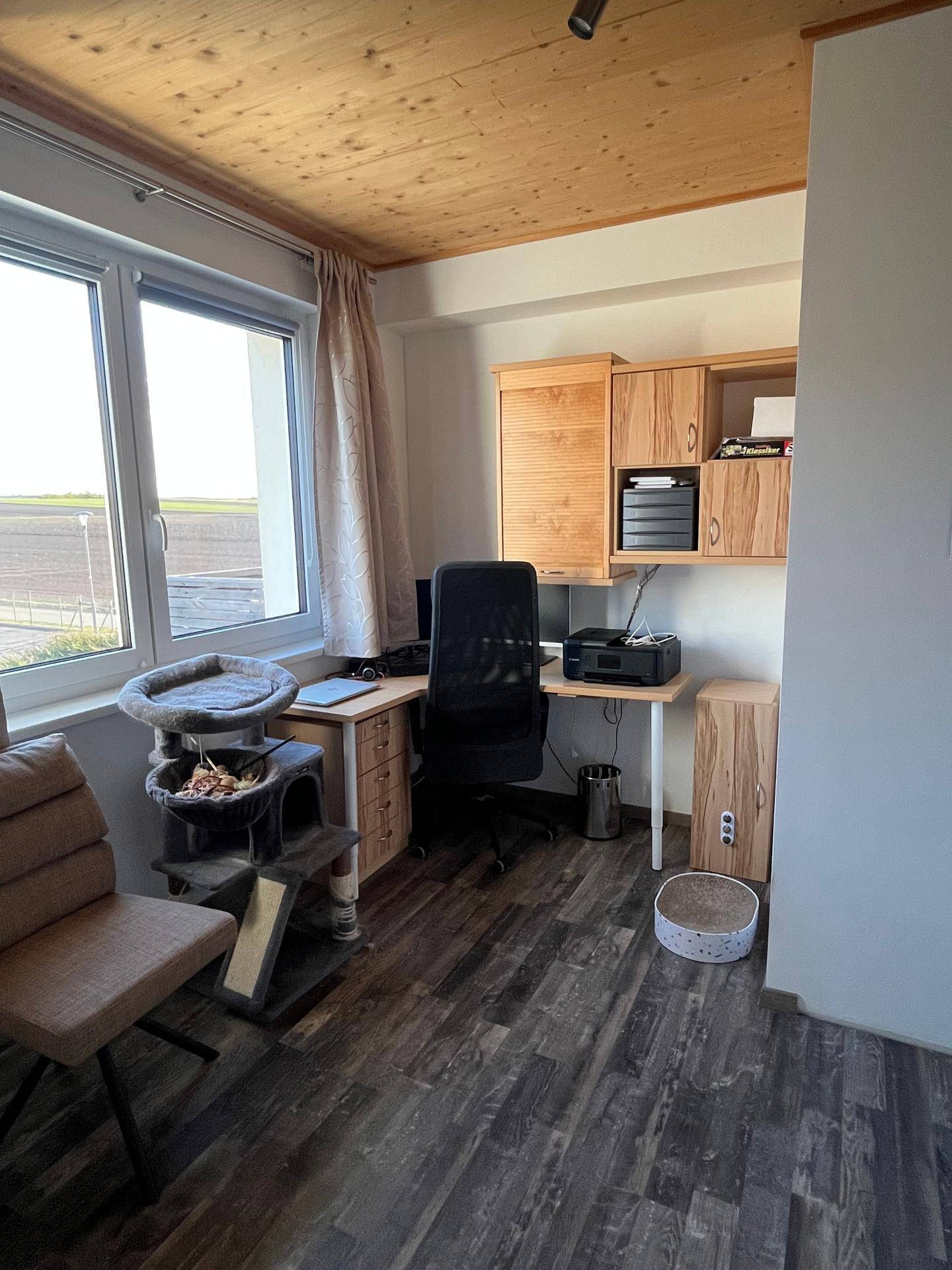 Helles Arbeitszimmer mit Holzdecke, Laminatboden und einem Schreibtisch am Fenster.