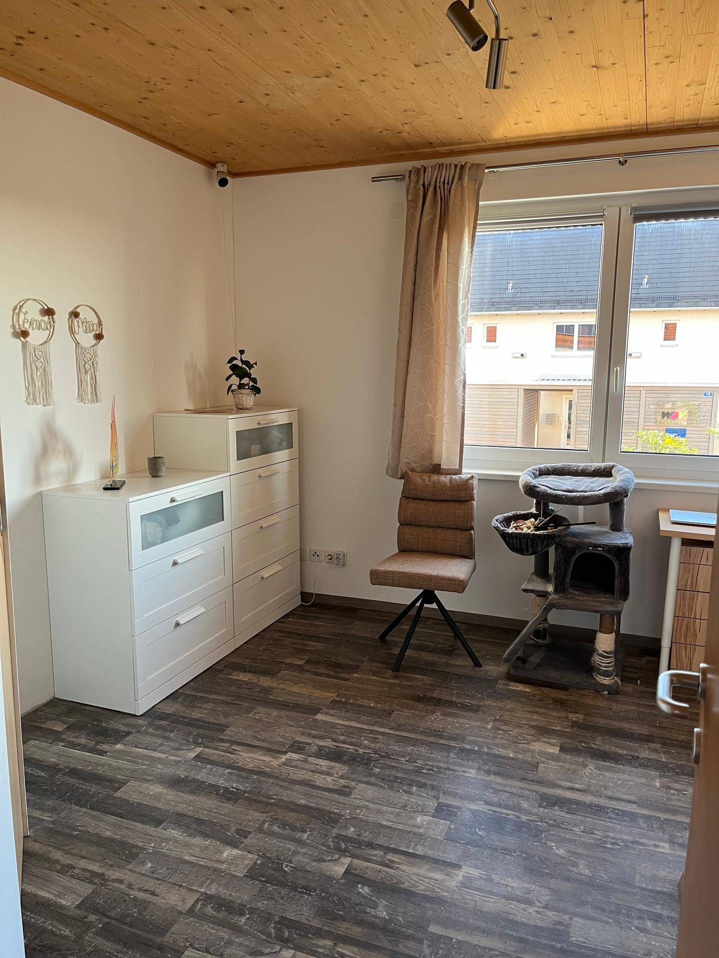 Schlafzimmer mit Holzdecke, Laminatboden und einem Fenster mit Blick ins Grüne.