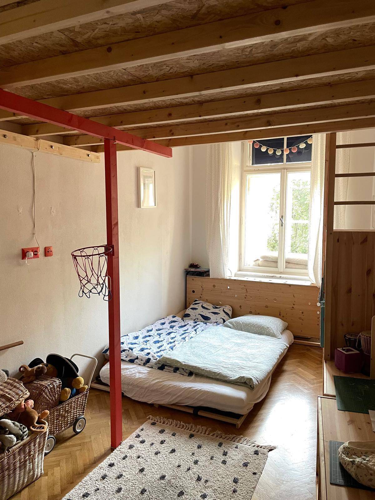 Kinderzimmer mit Holzboden, Hochbettkonstruktion und einem Fenster für natürliches Licht.