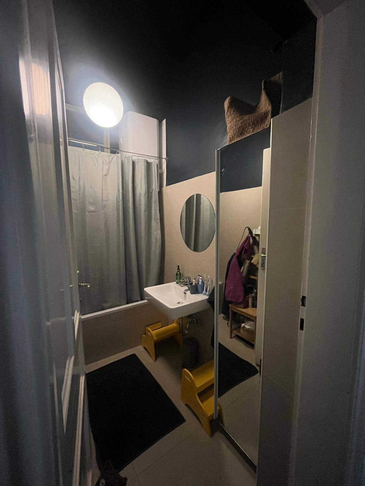 Kleines Badezimmer mit Badewanne, Waschbecken und einem runden Spiegel.