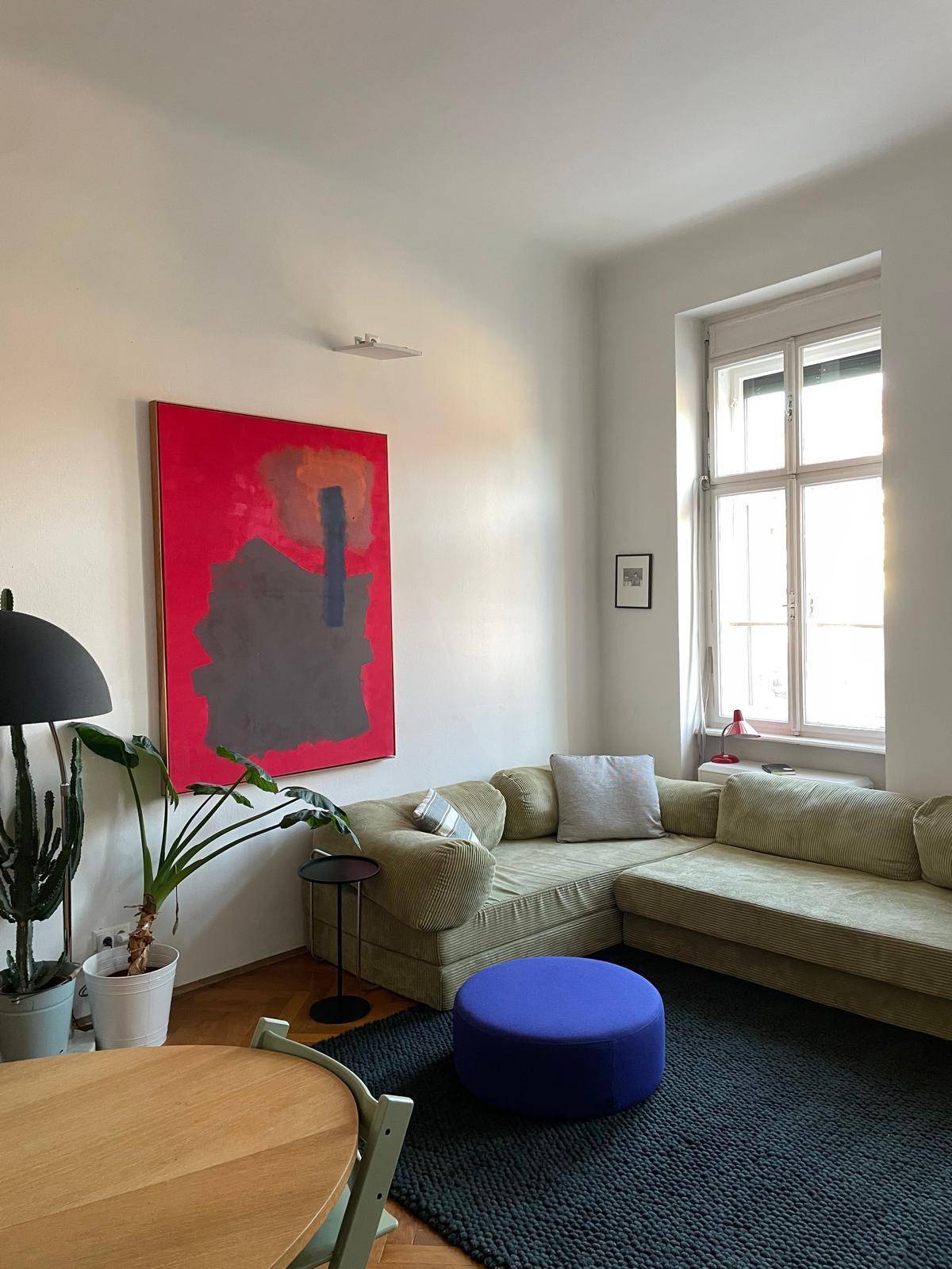 Helles Wohnzimmer mit beigem Ecksofa, farbenfrohem Kunstwerk und Holzboden.