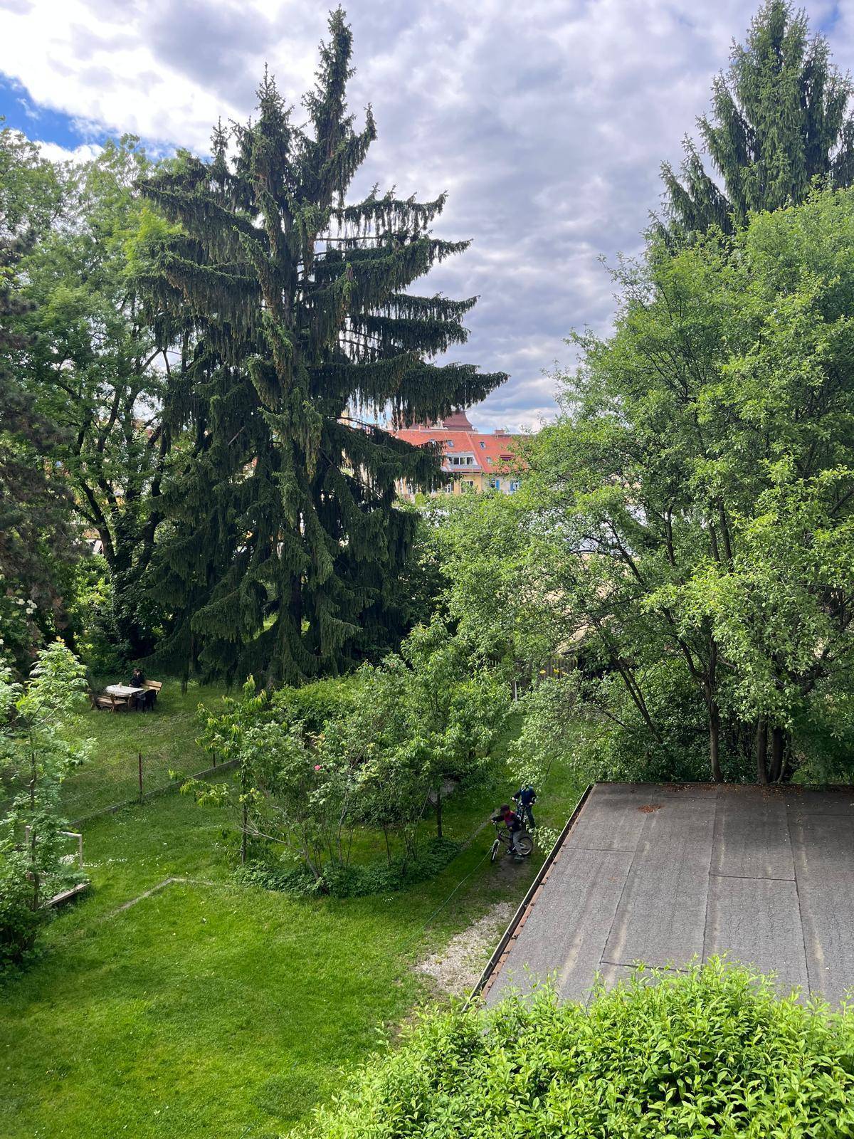 Blick von oben auf einen grünen Gemeinschaftsgarten mit hohen Bäumen und spielenden Kindern.