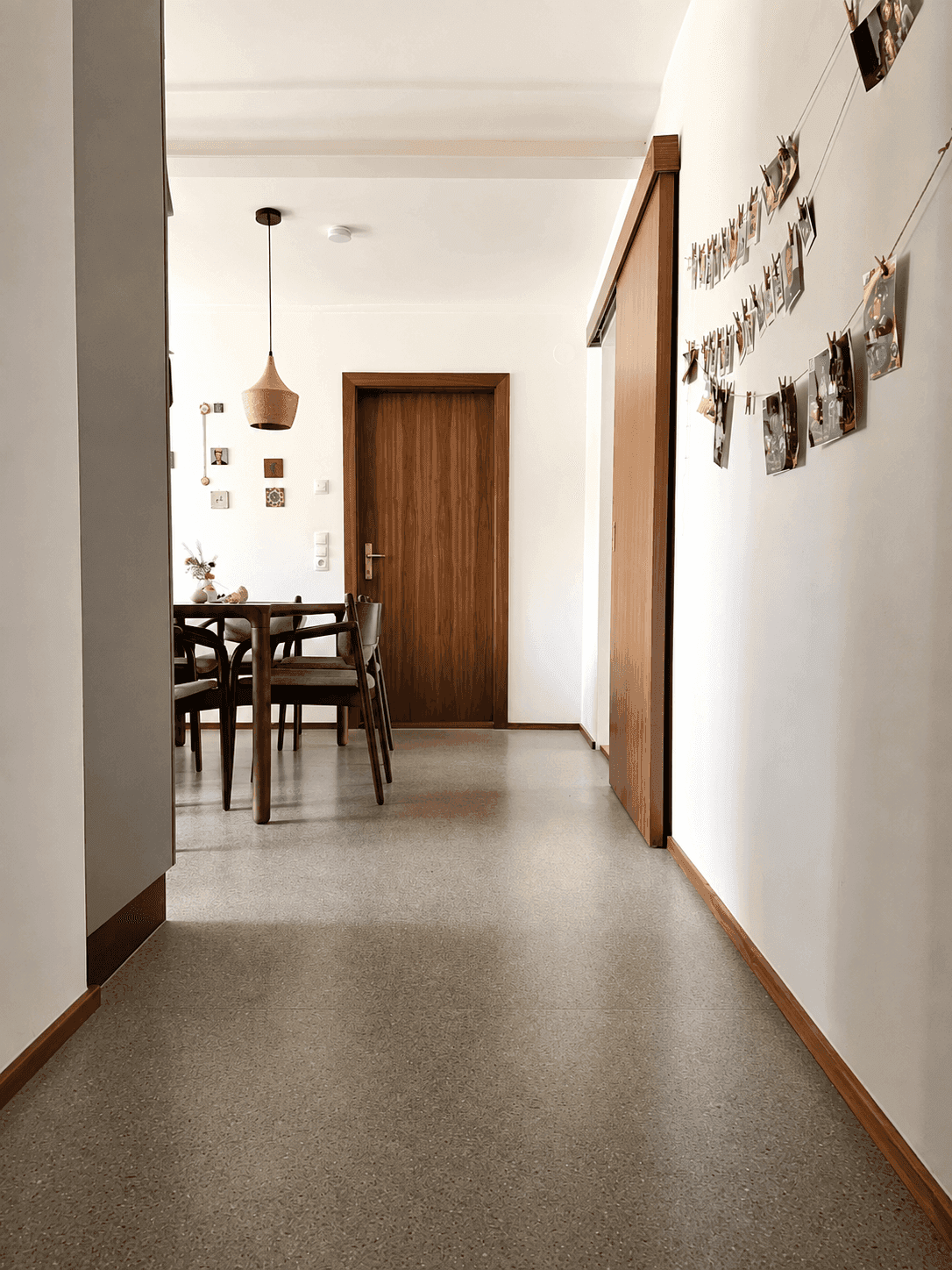 Heller Flur mit Terrazzoboden, der zu einem Essbereich mit Holztisch führt.