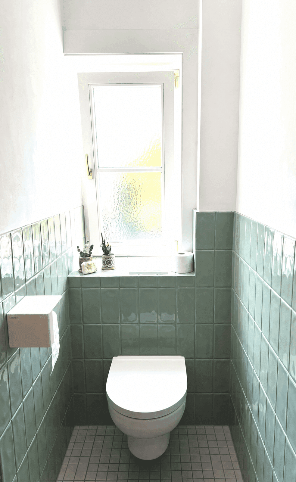 Helles Gäste-WC mit Fenster, Wand-WC und mintgrünen Fliesen an den Wänden.