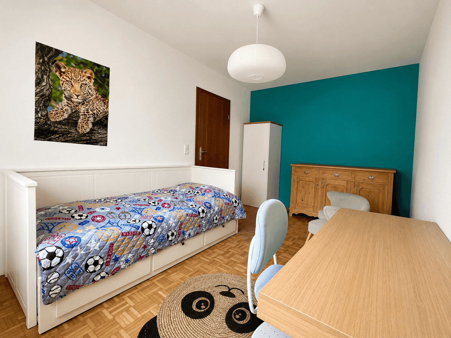 Kinderzimmer mit Einzelbett, Schreibtisch und farbenfroher Dekoration an der Wand.