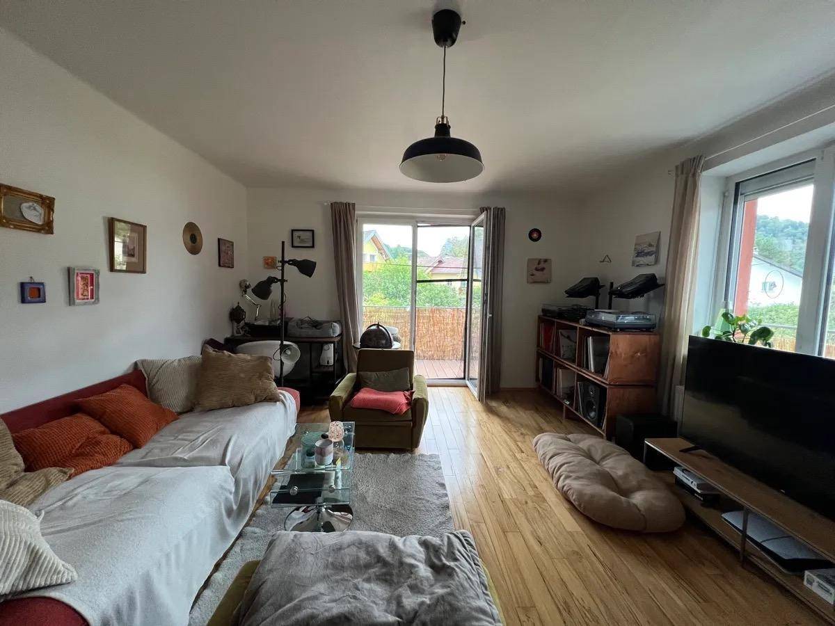 Helles Wohnzimmer mit Sofa, Fernseher und direktem Zugang zum Balkon.