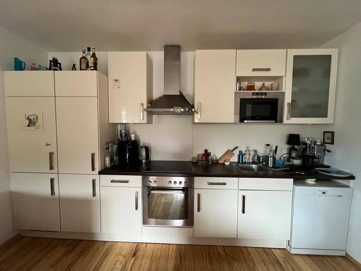 Moderne Einbauküche mit weißen Schränken, integrierten Geräten und dunkler Arbeitsplatte.