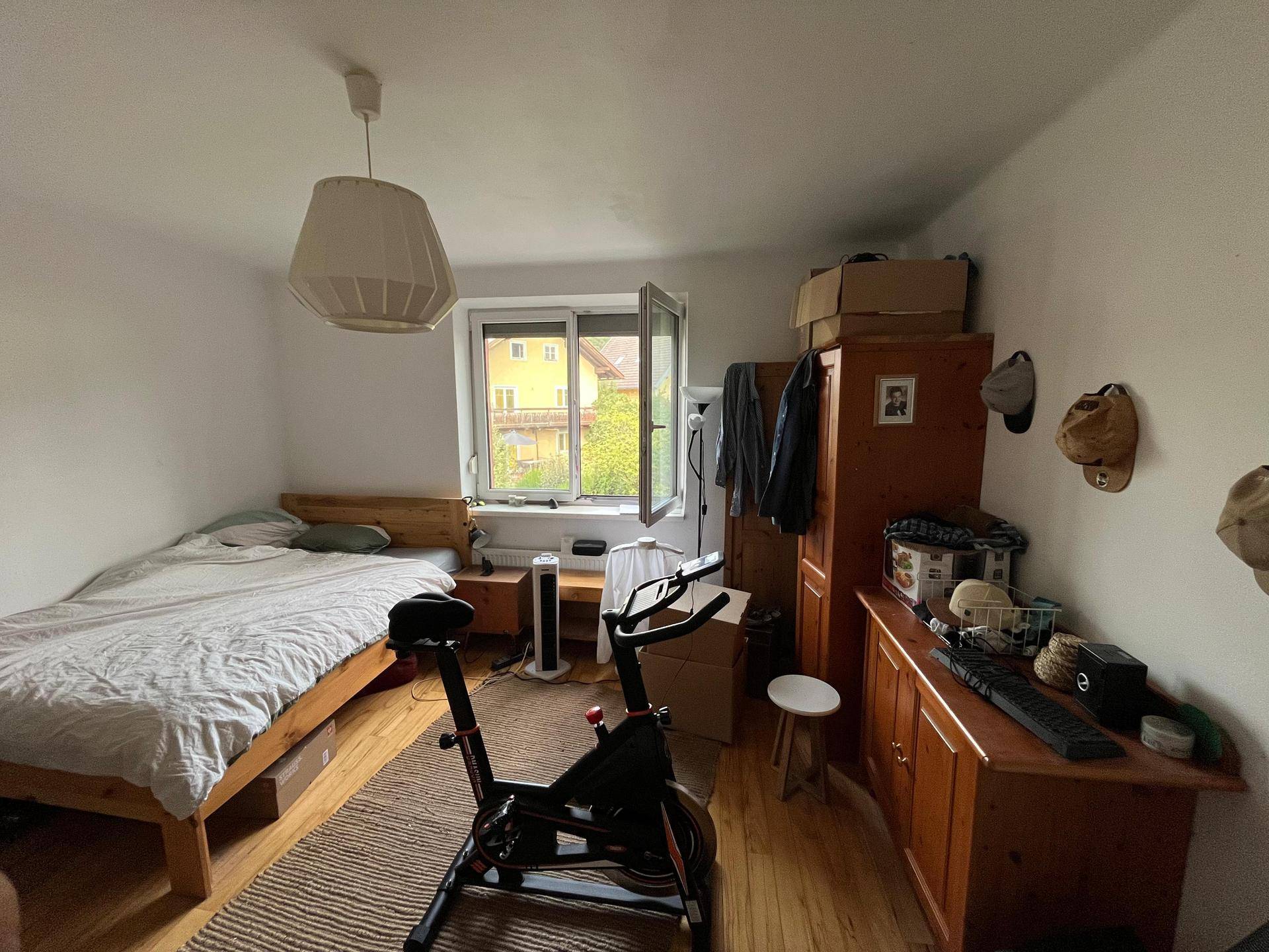 Schlafzimmer mit Holzbett, Kleiderschrank und einem Fenster mit Blick ins Grüne.