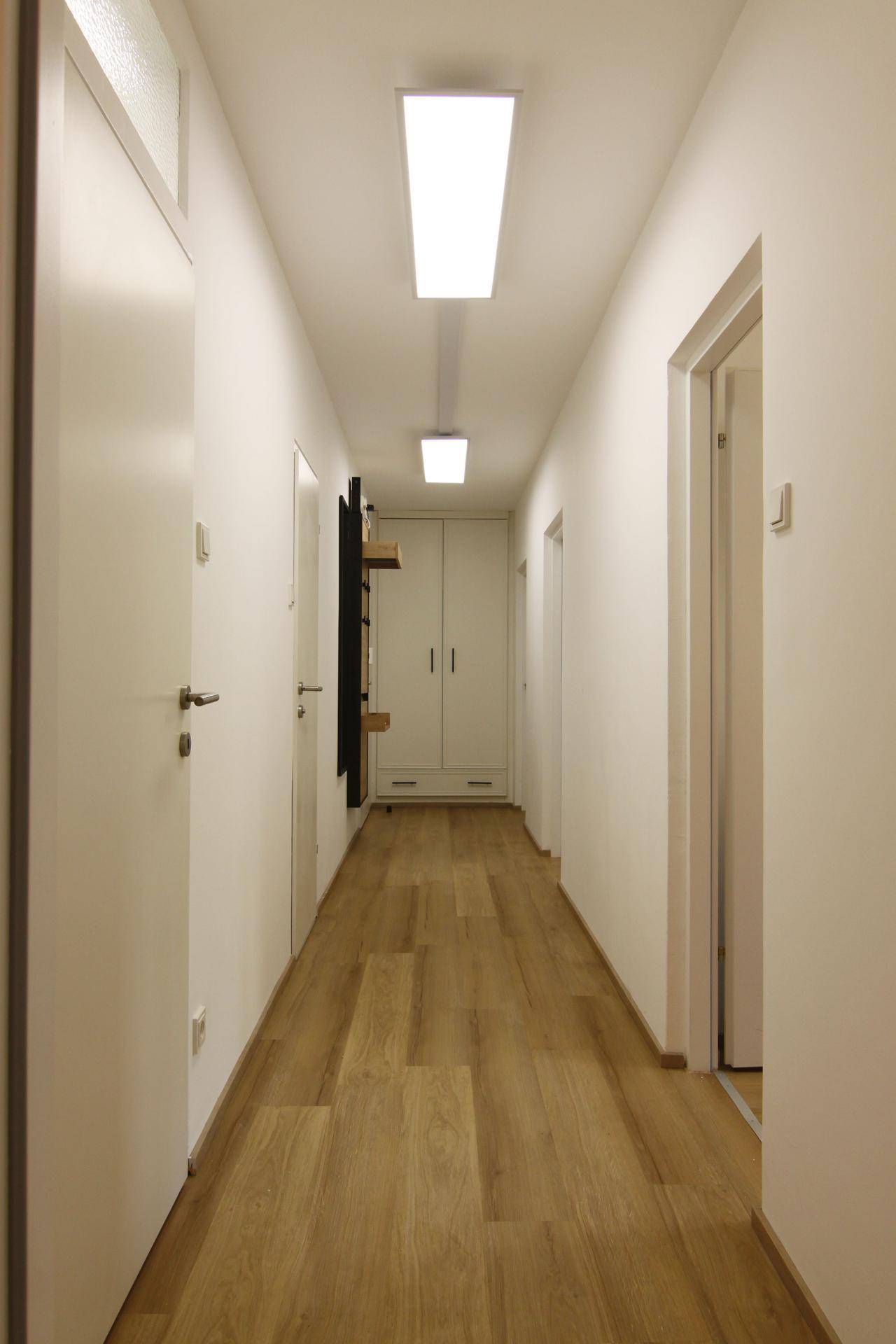 Langer, heller Flur mit Laminatboden und modernen Deckenleuchten, verbindet die Wohnbereiche.