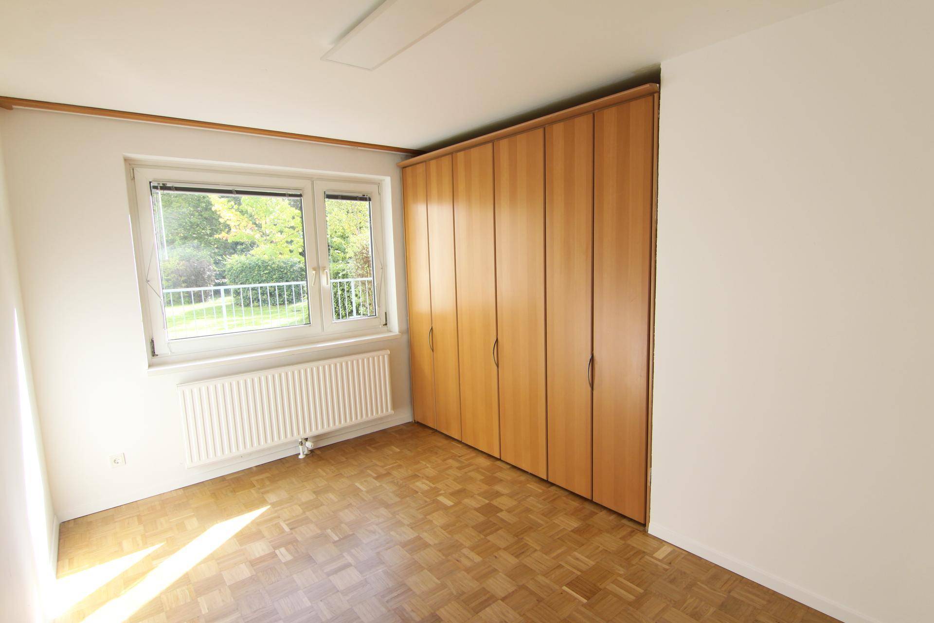 Helles Schlafzimmer mit Parkettboden, Einbauschrank und Blick ins Grüne, gut belichtet.