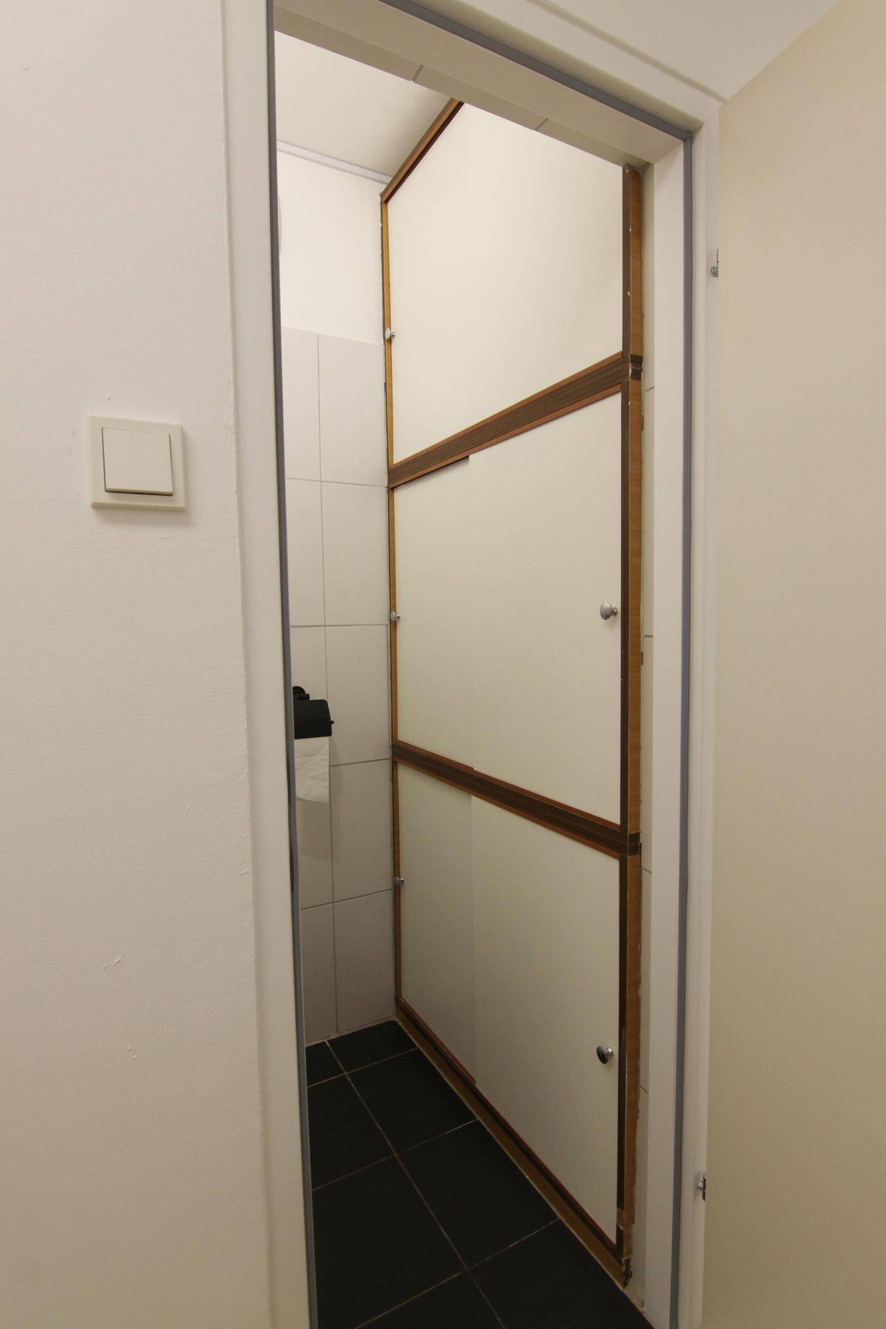 Blick in das kompakte separate WC mit Fliesenboden und weißen Wänden.