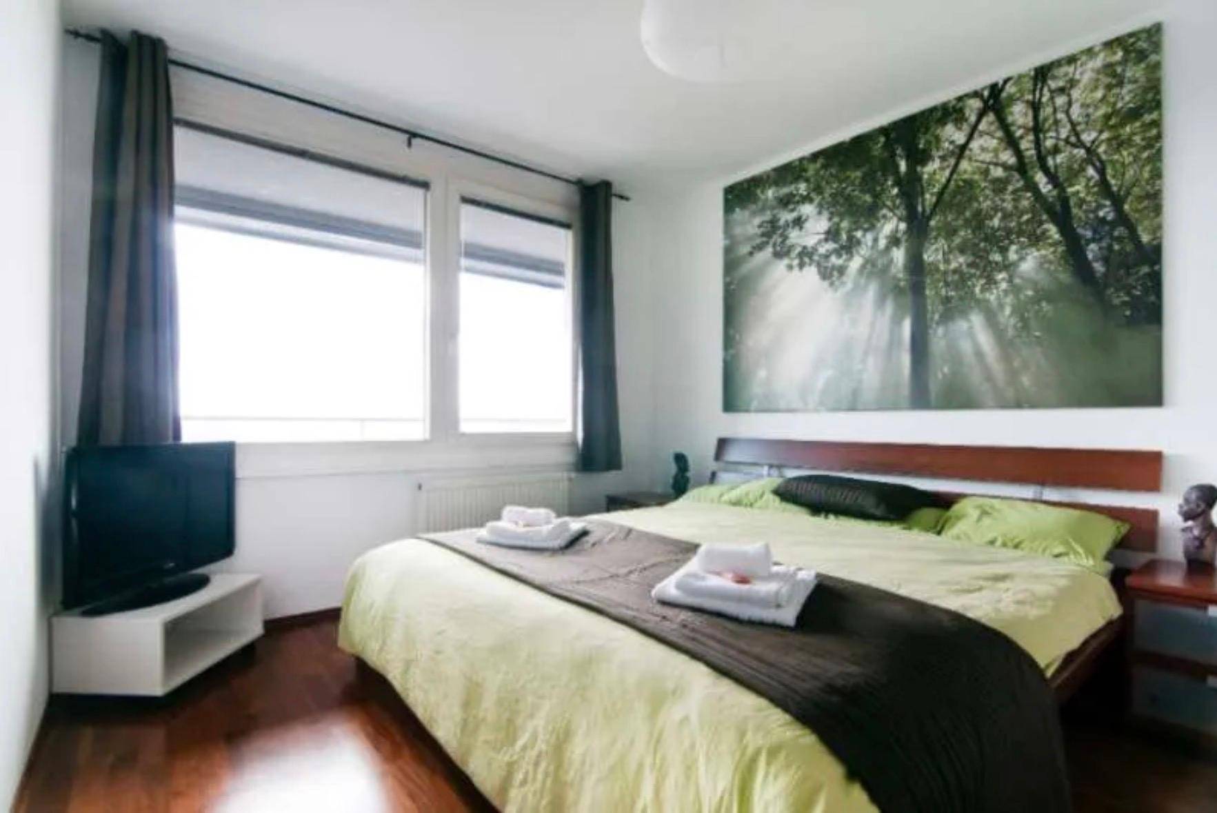 Helles Schlafzimmer mit Holzboden, großem Fenster und Waldmotiv an der Wand.