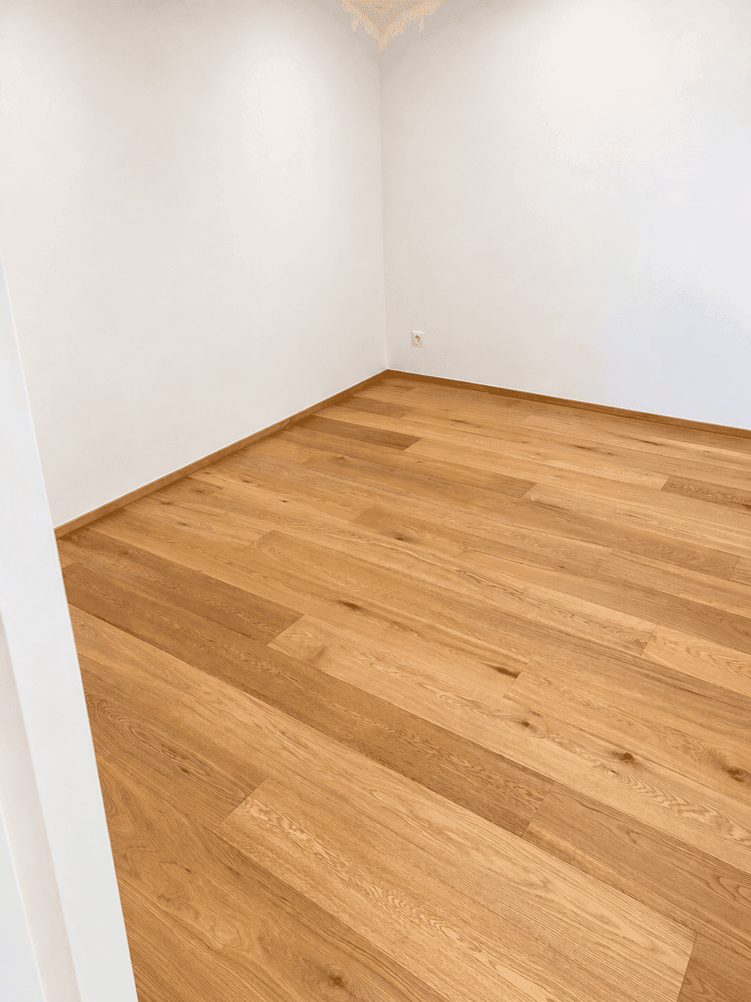 Leerer Raum mit hellem Holzparkettboden und weißen Wänden, bereit zur individuellen Gestaltung.