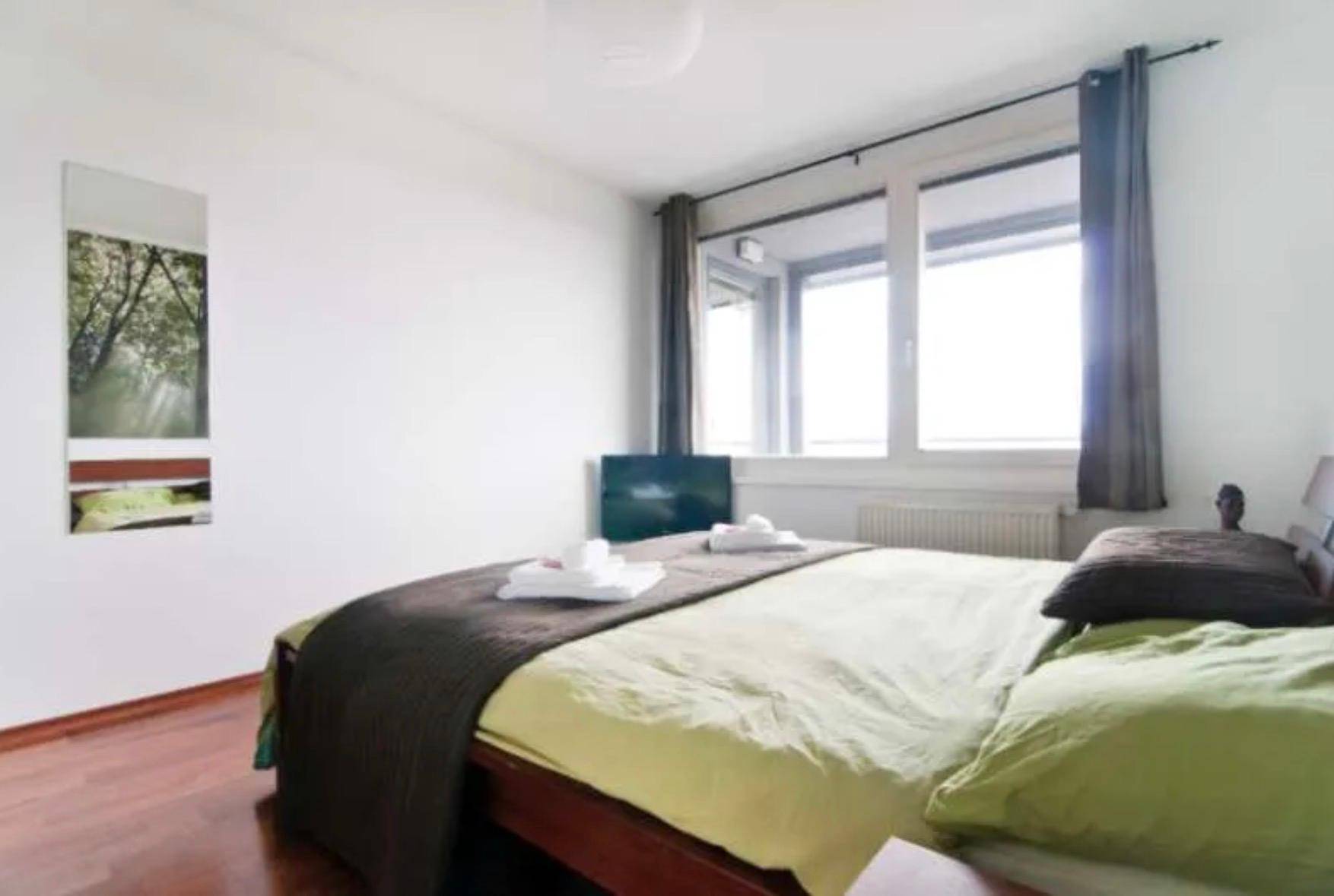 Schlafzimmer mit Holzboden, großem Fenster und grüner Bettwäsche.