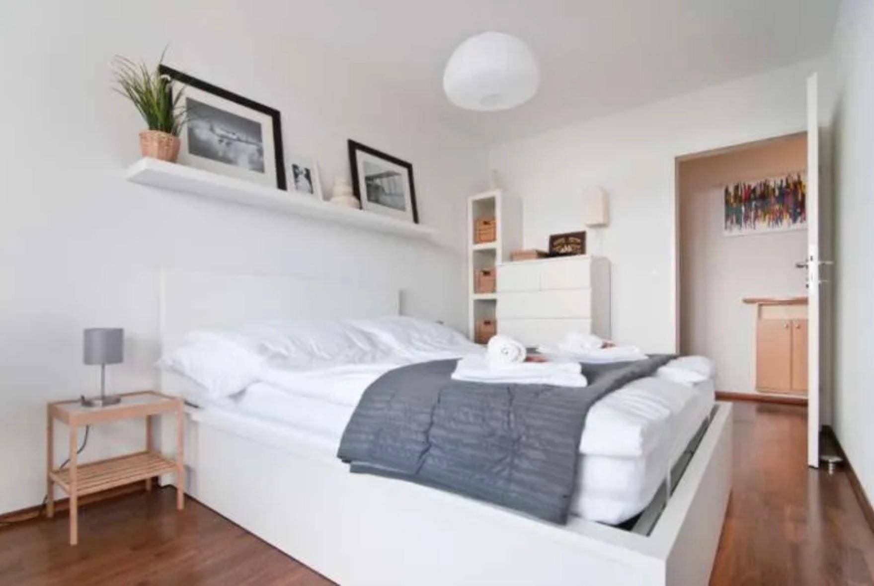 Schlafzimmer mit Holzboden, weißem Bett und minimalistischer Einrichtung.