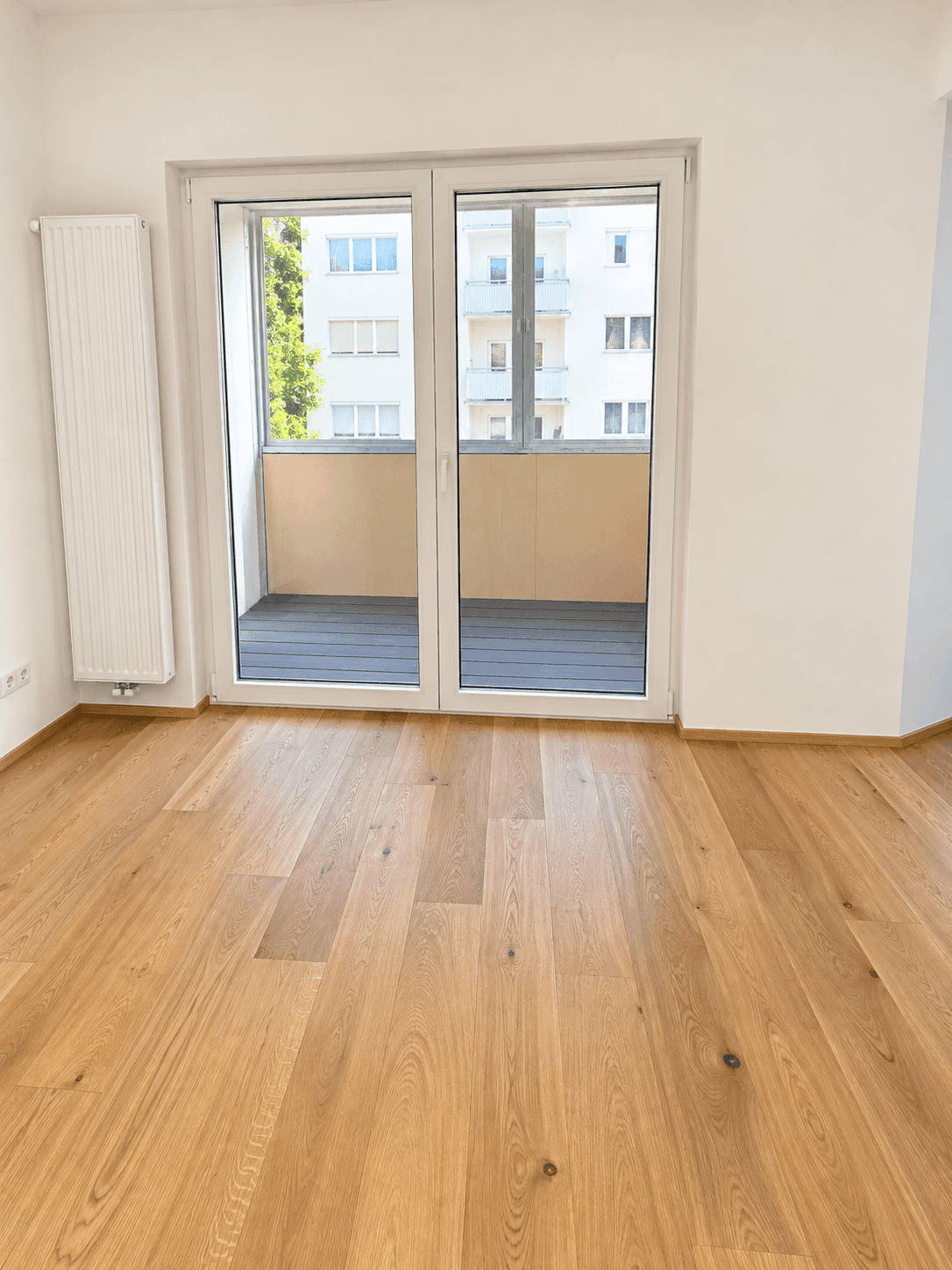 Heller Raum mit Holzparkettboden und Zugang zu einem kleinen Balkon, ideal für frische Luft.