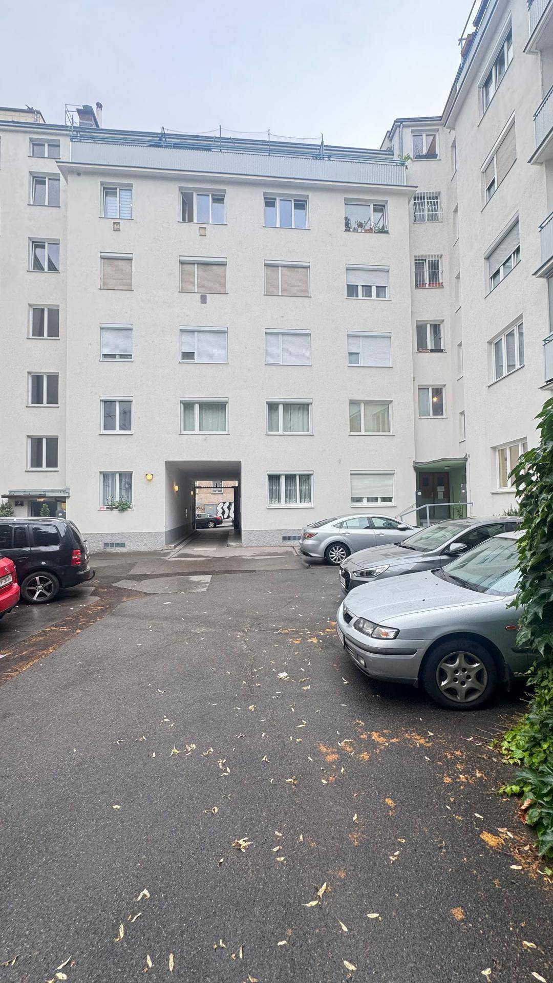 Innenhof eines Wohngebäudes mit geparkten Autos und Durchgang zu weiteren Bereichen.