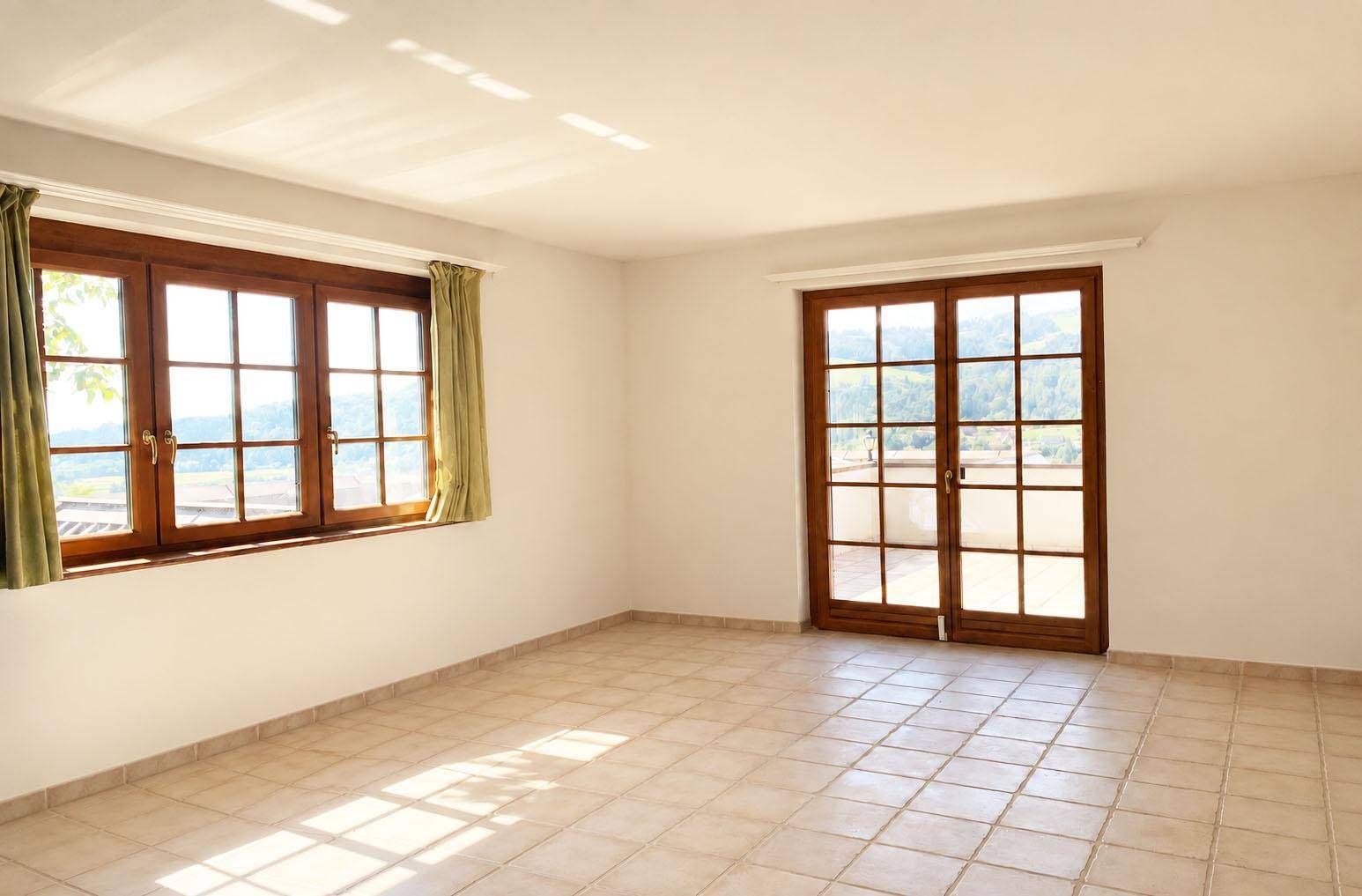 Geräumiger, leerer Raum mit Fliesenboden, Holzfenstern und Balkonzugang, bietet viel natürliches Licht.