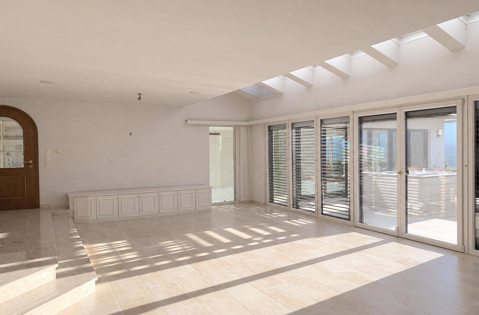Heller, leerer Raum mit großen Glasfronten, Oberlichtern und Fliesenboden, ideal für einen Wohnbereich.