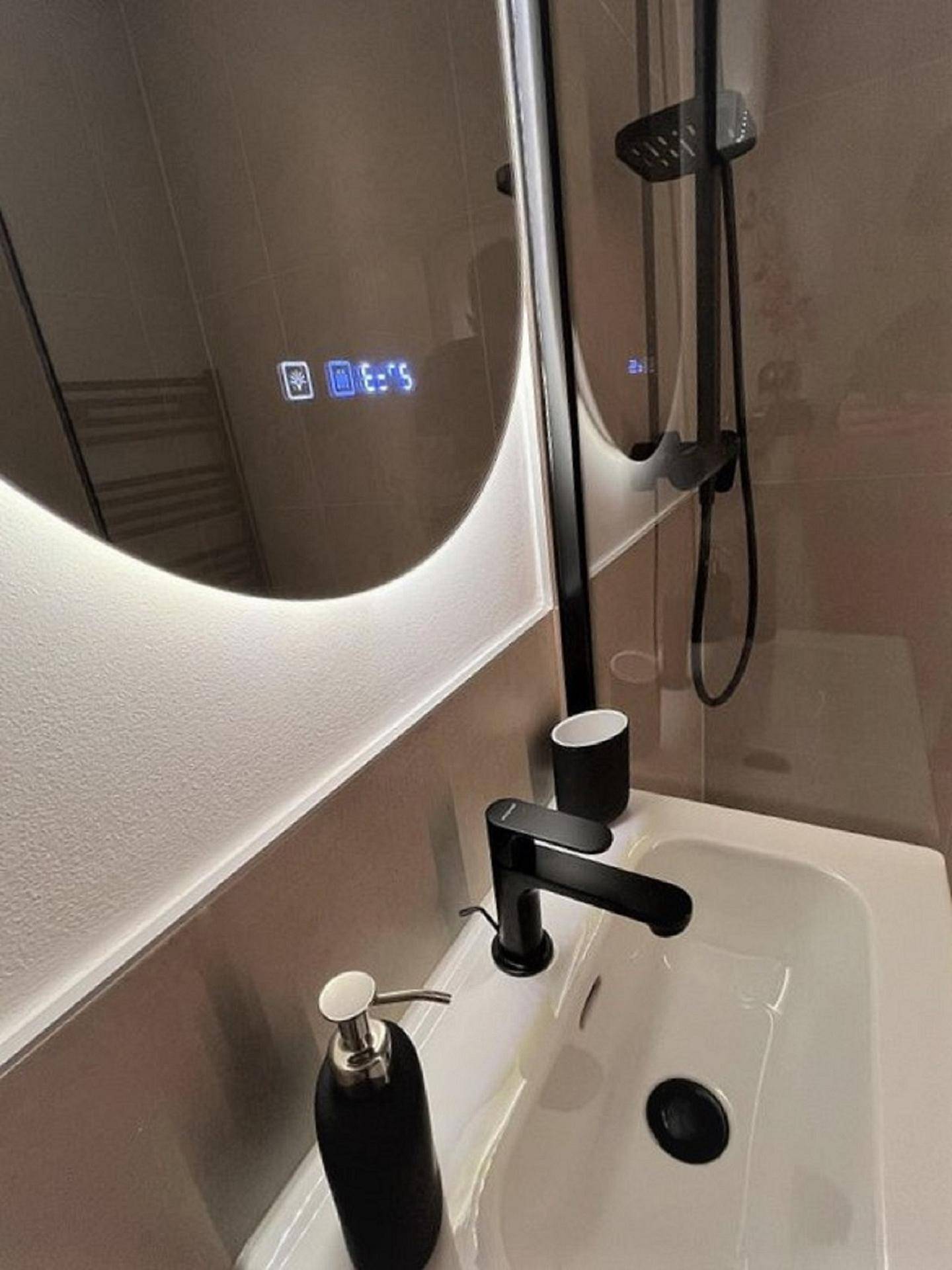 Detailansicht des modernen Waschbeckens mit schwarzer Armatur und beleuchtetem Spiegel.