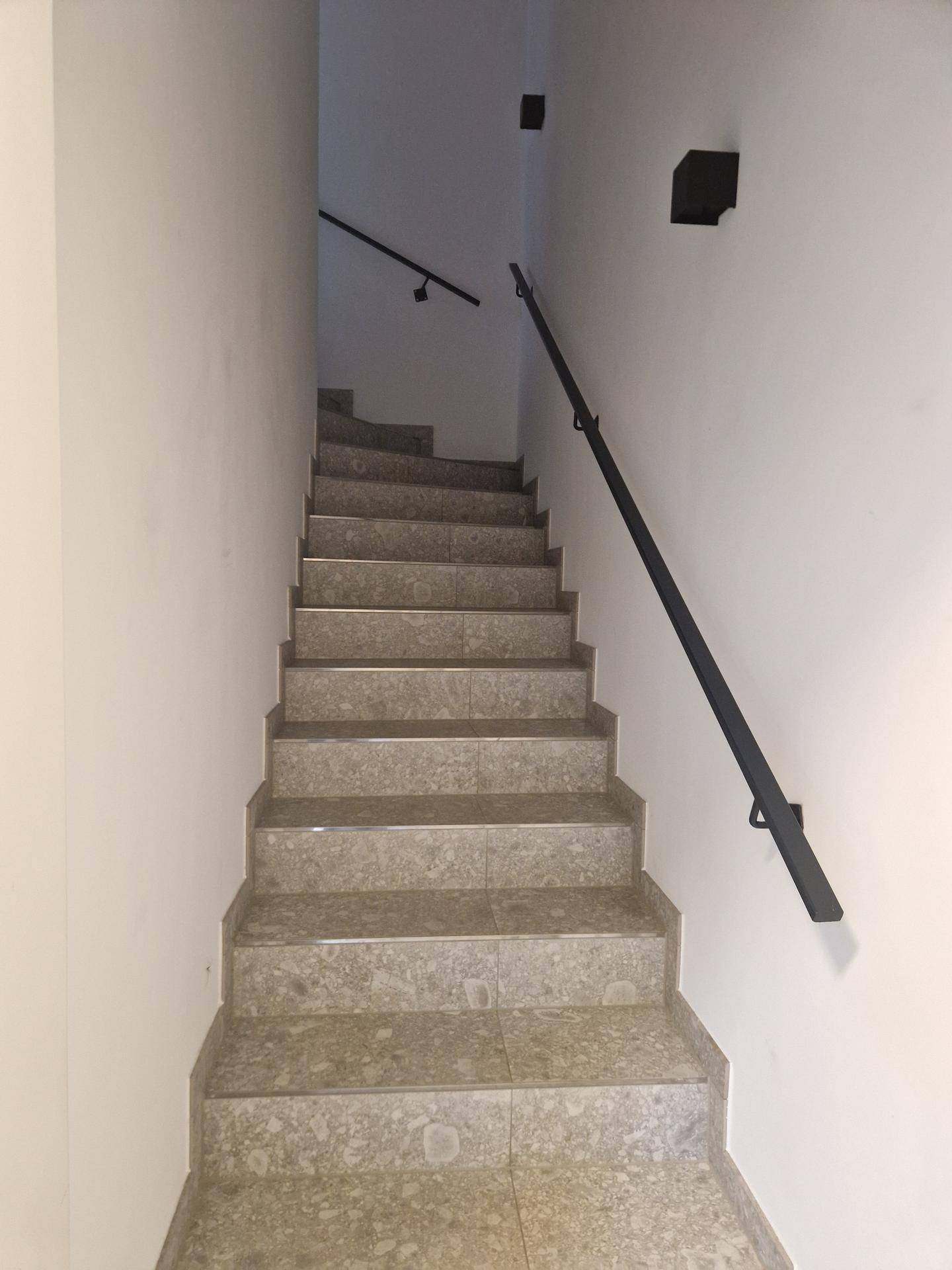 Treppenhaus mit gefliesten Stufen und schwarzem Handlauf, das die Etagen verbindet.