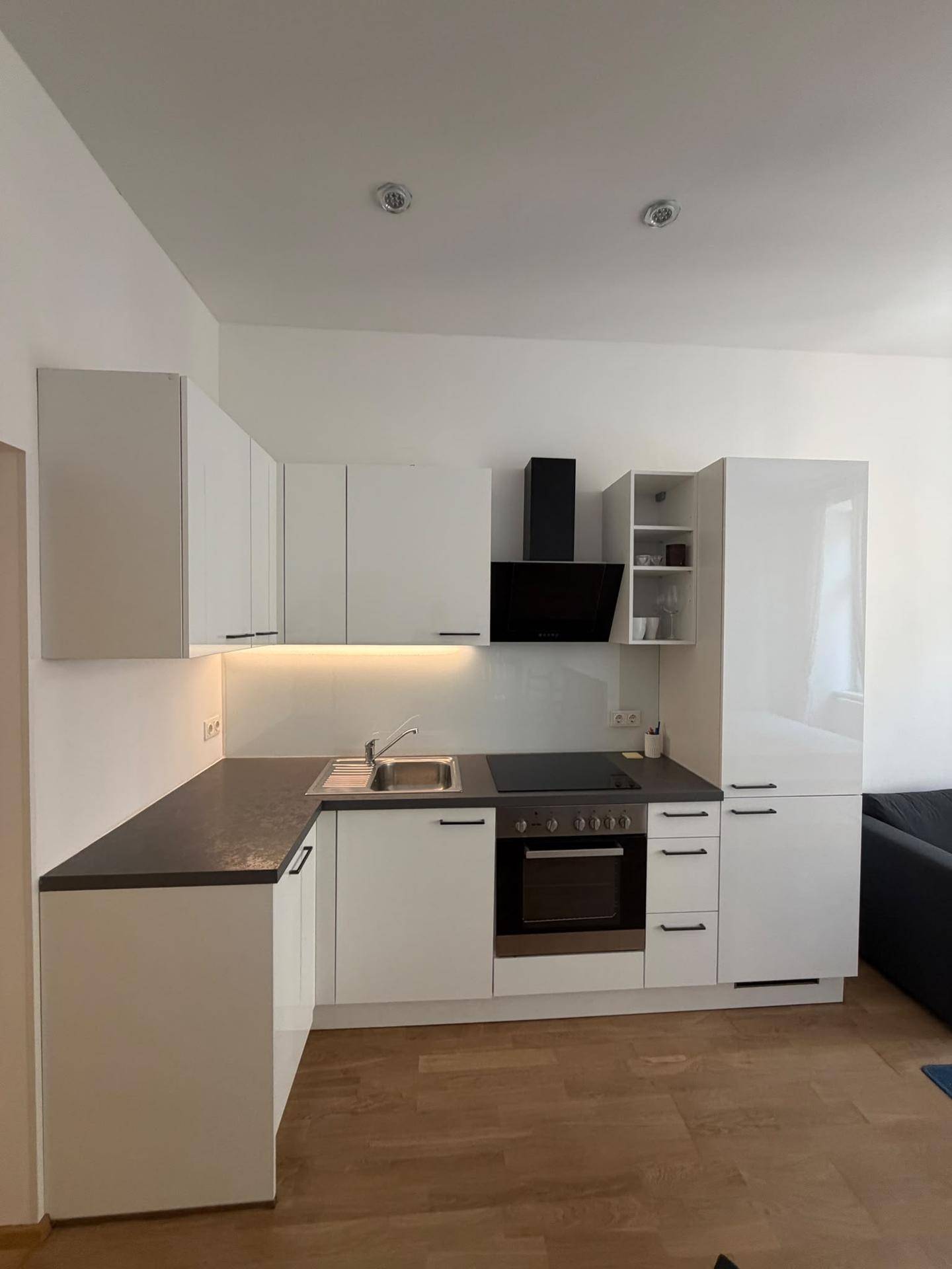 Moderne Einbauküche mit weißen Hochglanzfronten, integrierten Geräten und dunkler Arbeitsplatte.