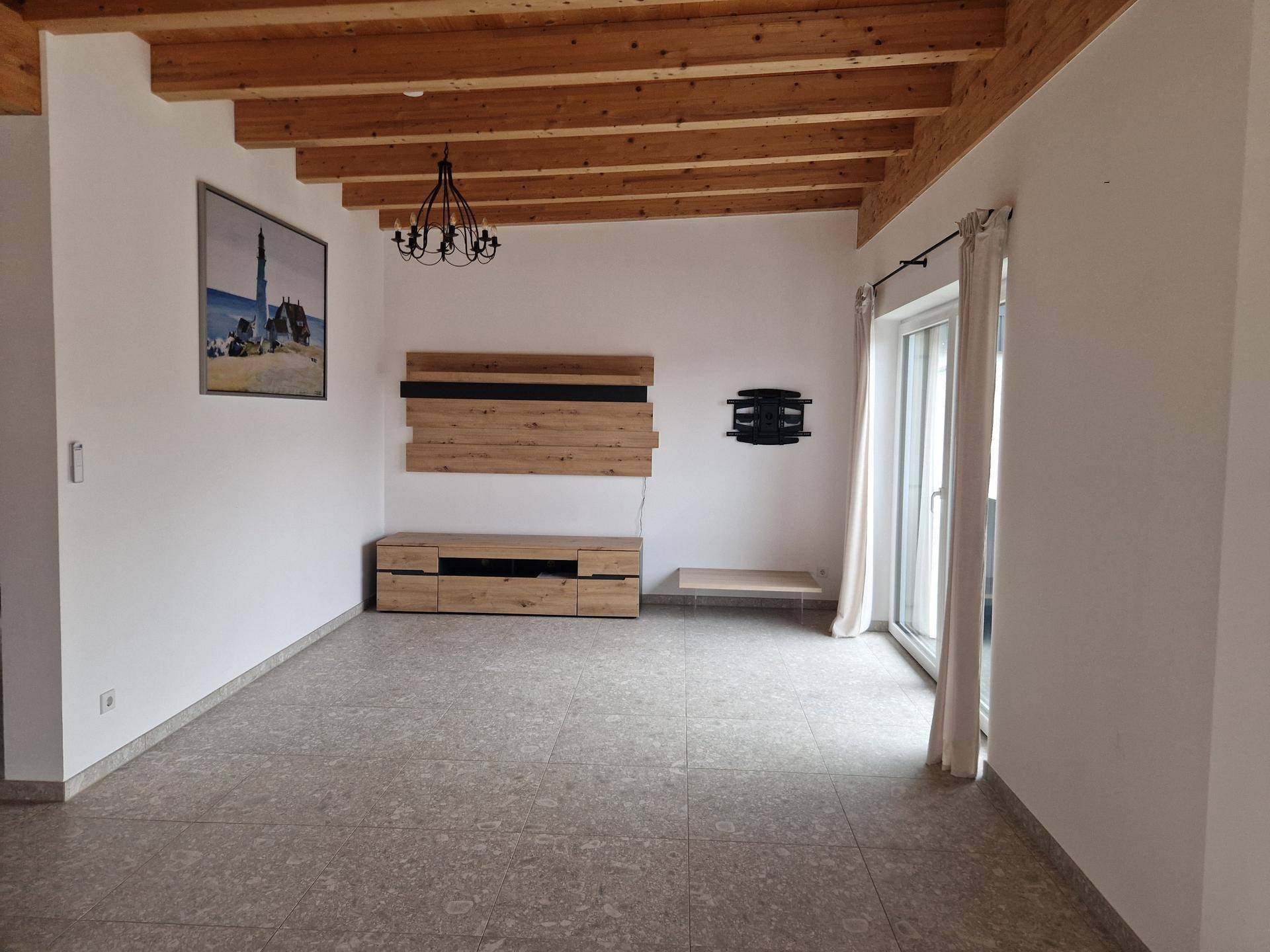Geräumiger Wohnbereich mit Fliesenboden, Holzbalkendecke und Zugang zu einem Außenbereich.
