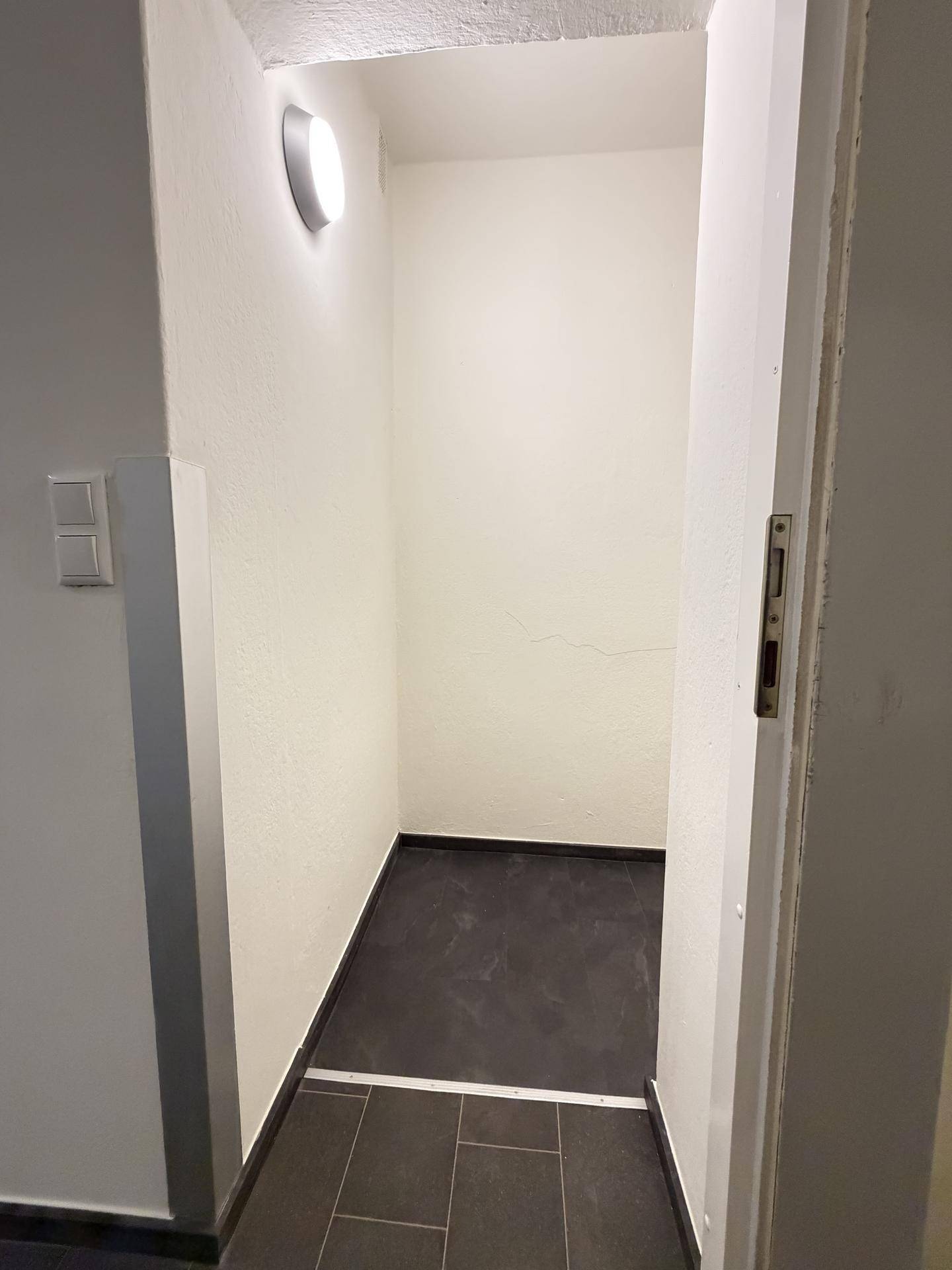 Kleiner Abstellraum oder Nische mit dunklem Fliesenboden und hellen Wänden.