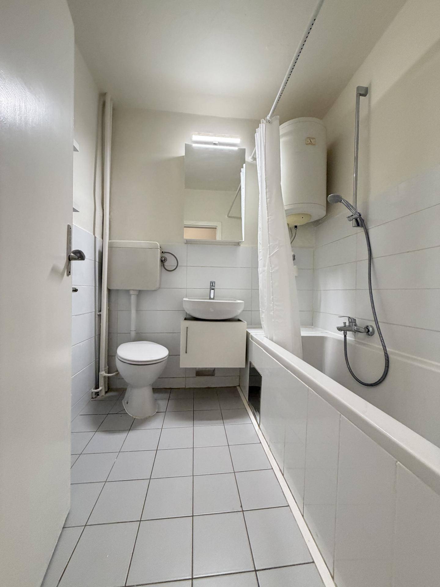 Badezimmer mit Badewanne, Toilette, Einzelwaschbecken und weißen Fliesen an den Wänden.