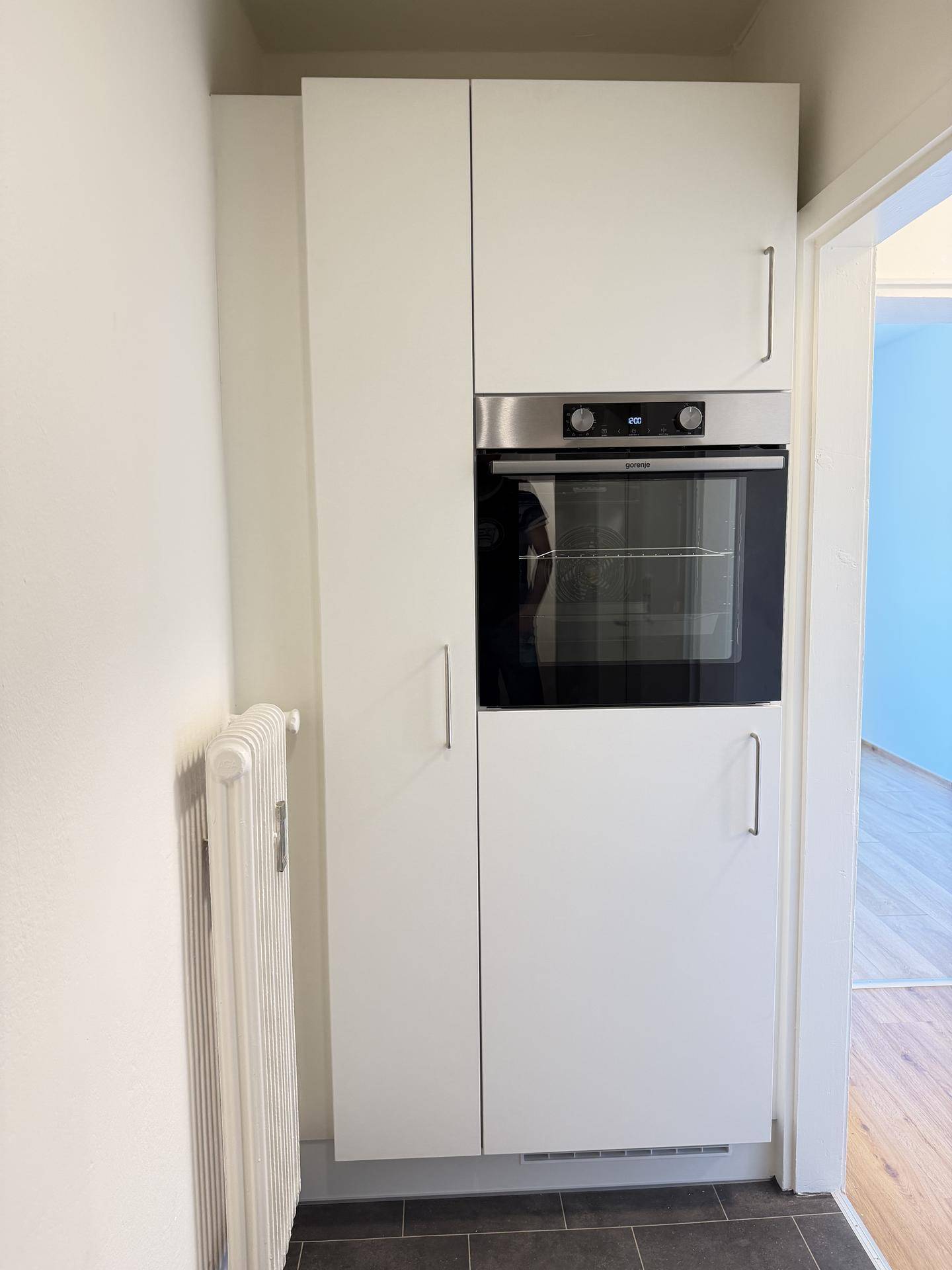 Integrierter Backofen in einer modernen weißen Küchenzeile mit Heizkörper im Vordergrund.