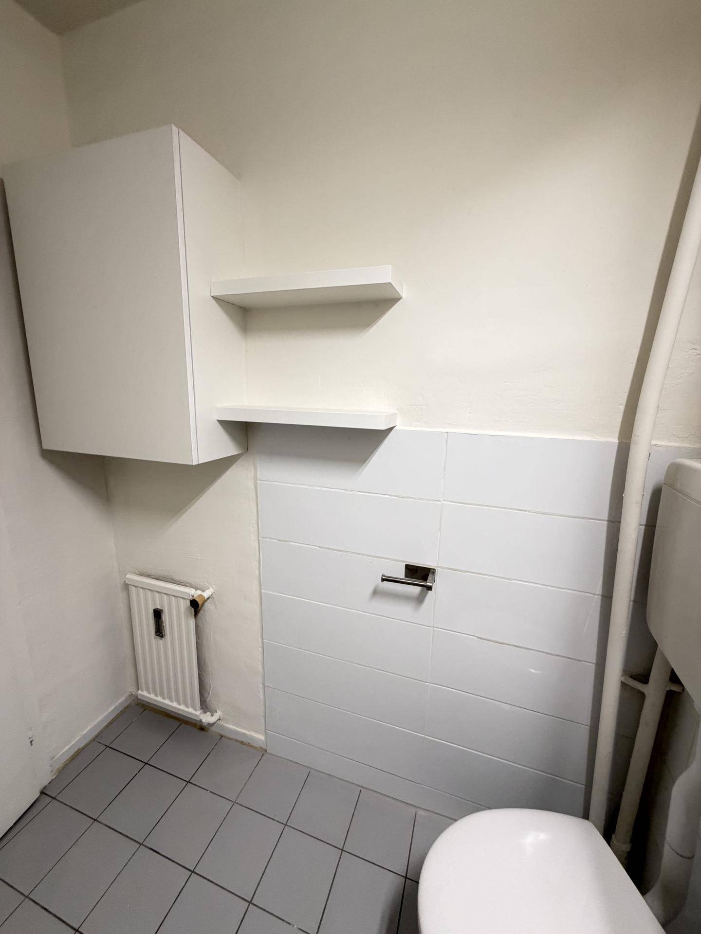 Kleines Gäste-WC mit Toilette, Heizkörper und weißen Wandfliesen auf dunklem Fliesenboden.