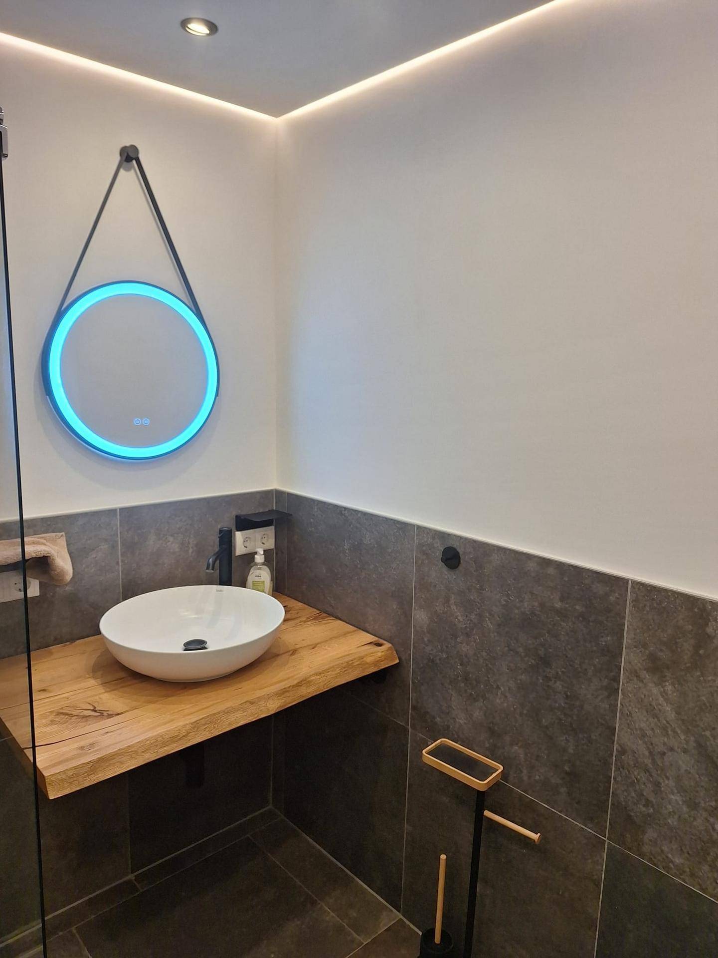 Modernes Badezimmer mit Aufsatzwaschbecken, Holzplatte und beleuchtetem Spiegel.