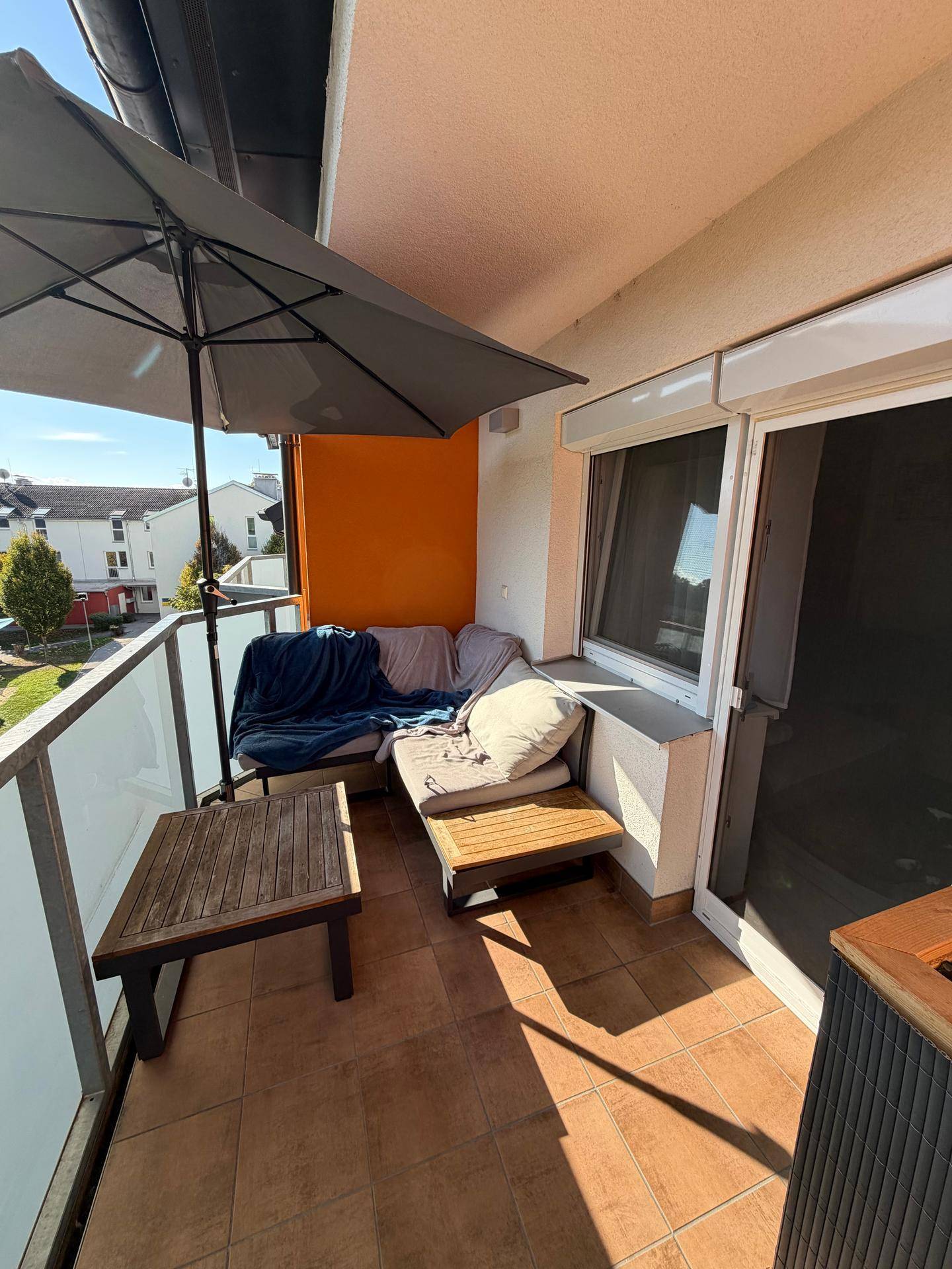 Sonniger Balkon mit bequemen Gartenmöbeln, Sonnenschirm und Blick auf die Umgebung.