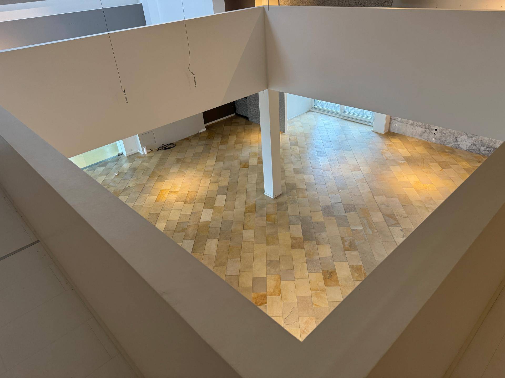 Blick von oben in den weitläufigen Gewerberaum mit Fliesenboden und Säulen, der viel Platz bietet.