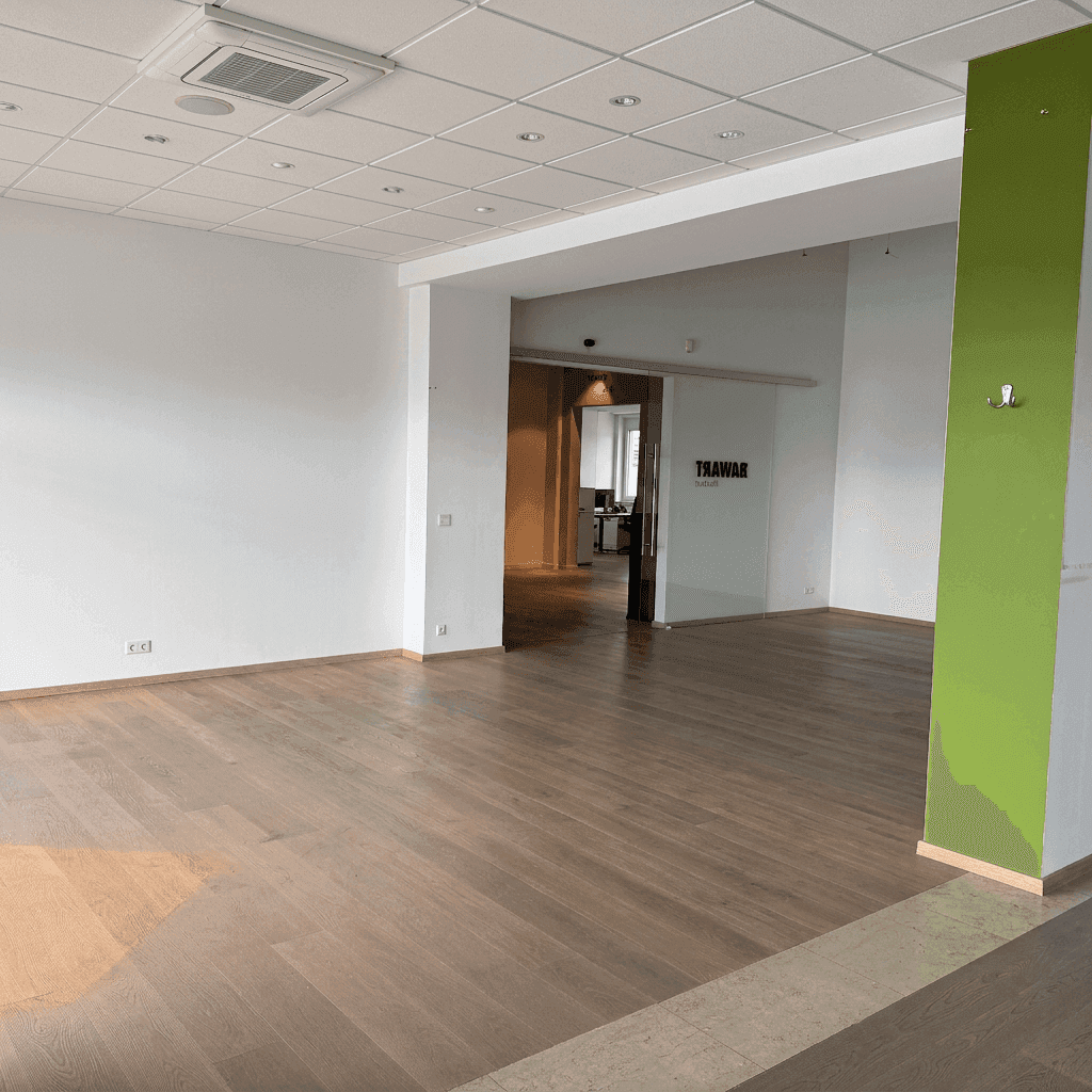 Heller Gewerberaum mit hellem Holzfußboden, weißen Wänden und grünem Akzent, ideal für Büros oder Studios.
