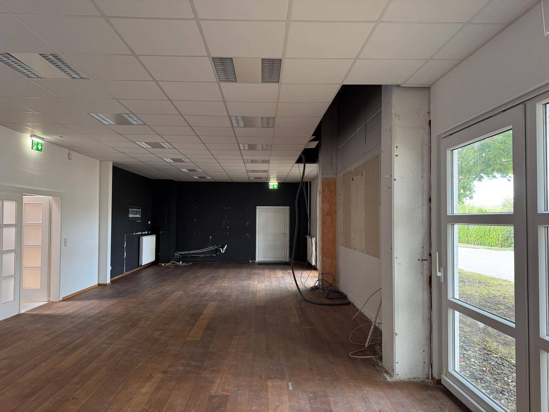 Leerer Gewerberaum mit dunklem Holzfußboden, abgehängter Decke und großen Fenstern, bereit zur Fertigstellung.