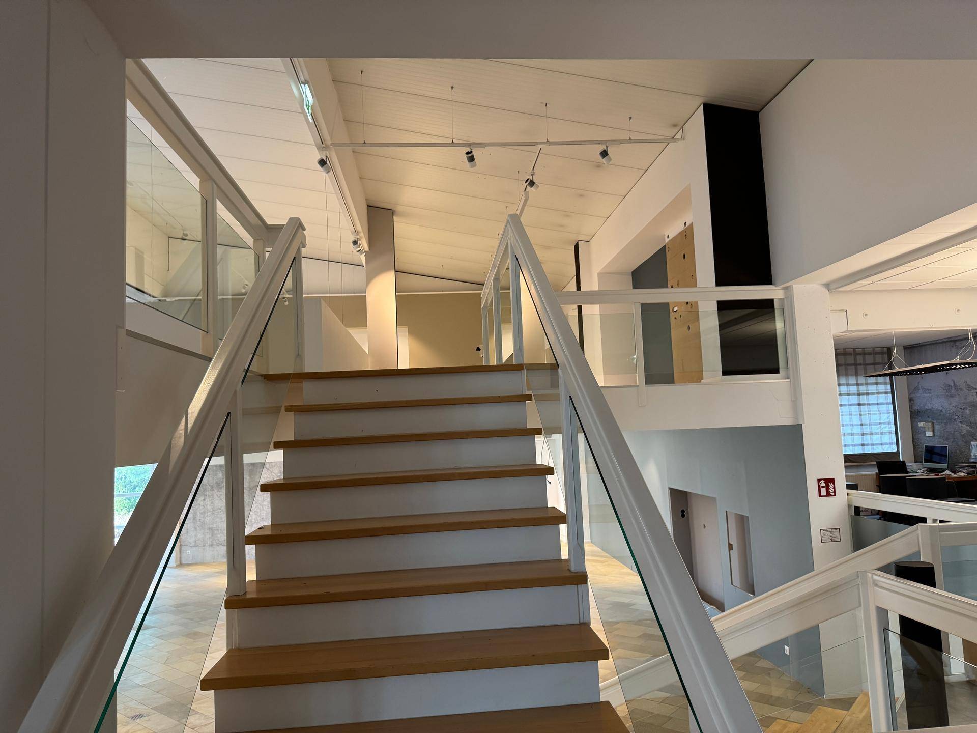 Moderne Treppe mit Holzstufen und Glasgeländer führt zu den oberen Etagen, beleuchtet von Deckenspots.