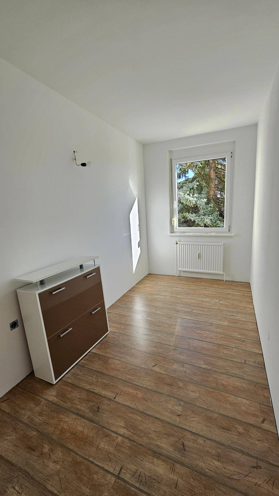 Kleines, helles Zimmer mit Laminatboden und einem Fenster, ideal als Kinder- oder Arbeitszimmer.