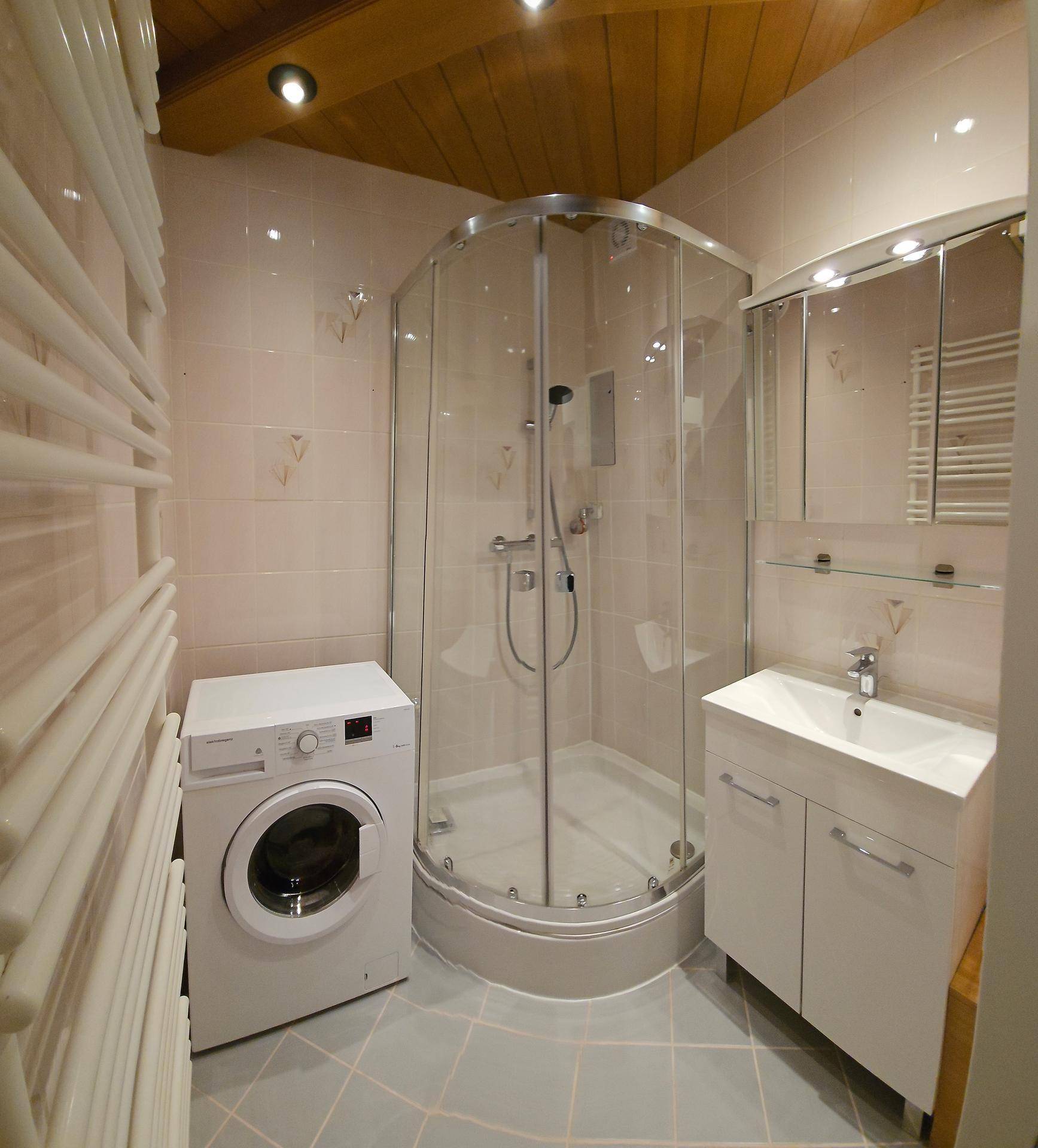 Modernes Badezimmer mit Duschkabine, Waschmaschine und beheiztem Handtuchhalter unter Holzdecke.
