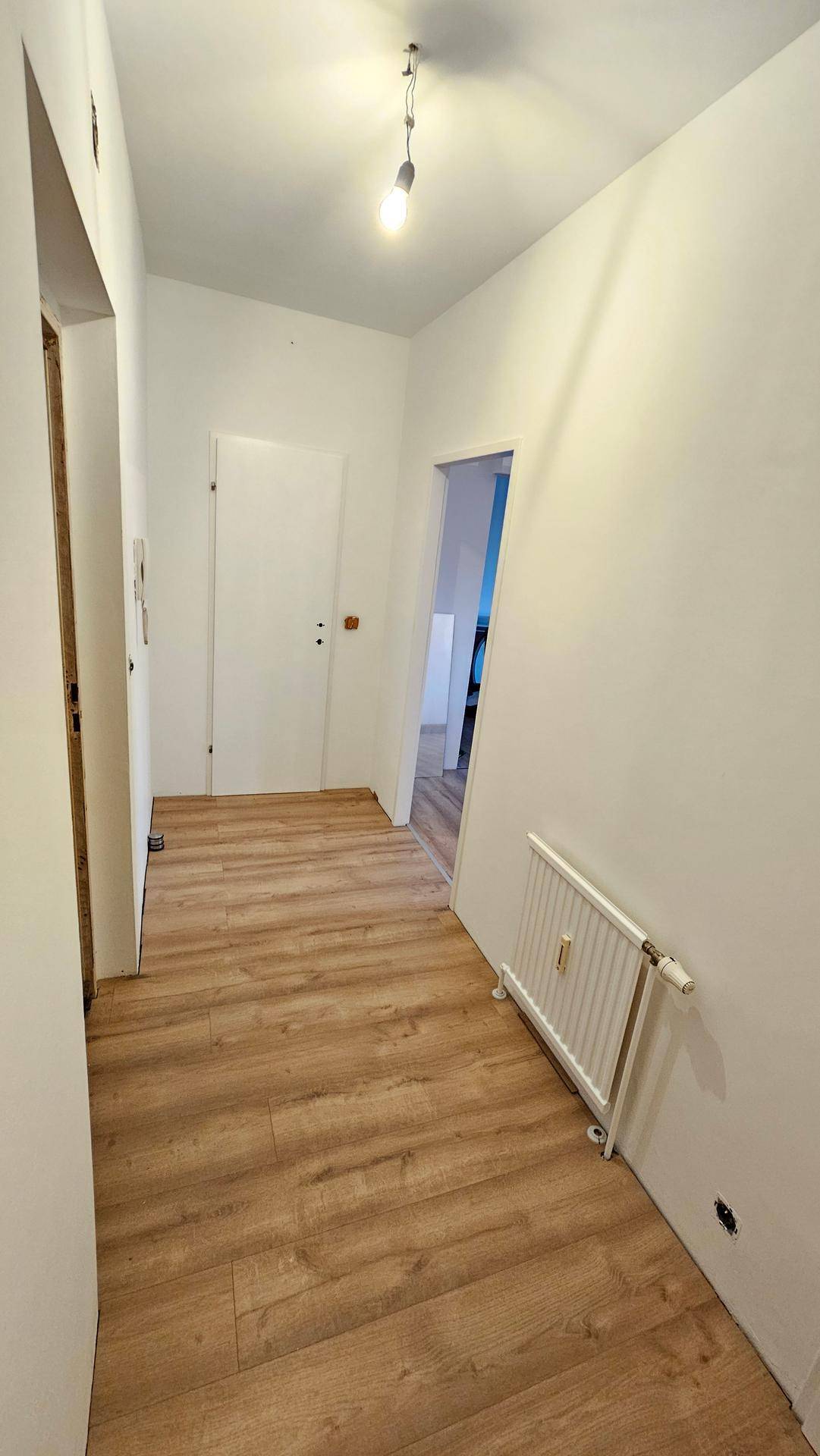 Heller Flur mit Laminatboden und weiß gestrichenen Wänden, der zu weiteren Räumen führt.