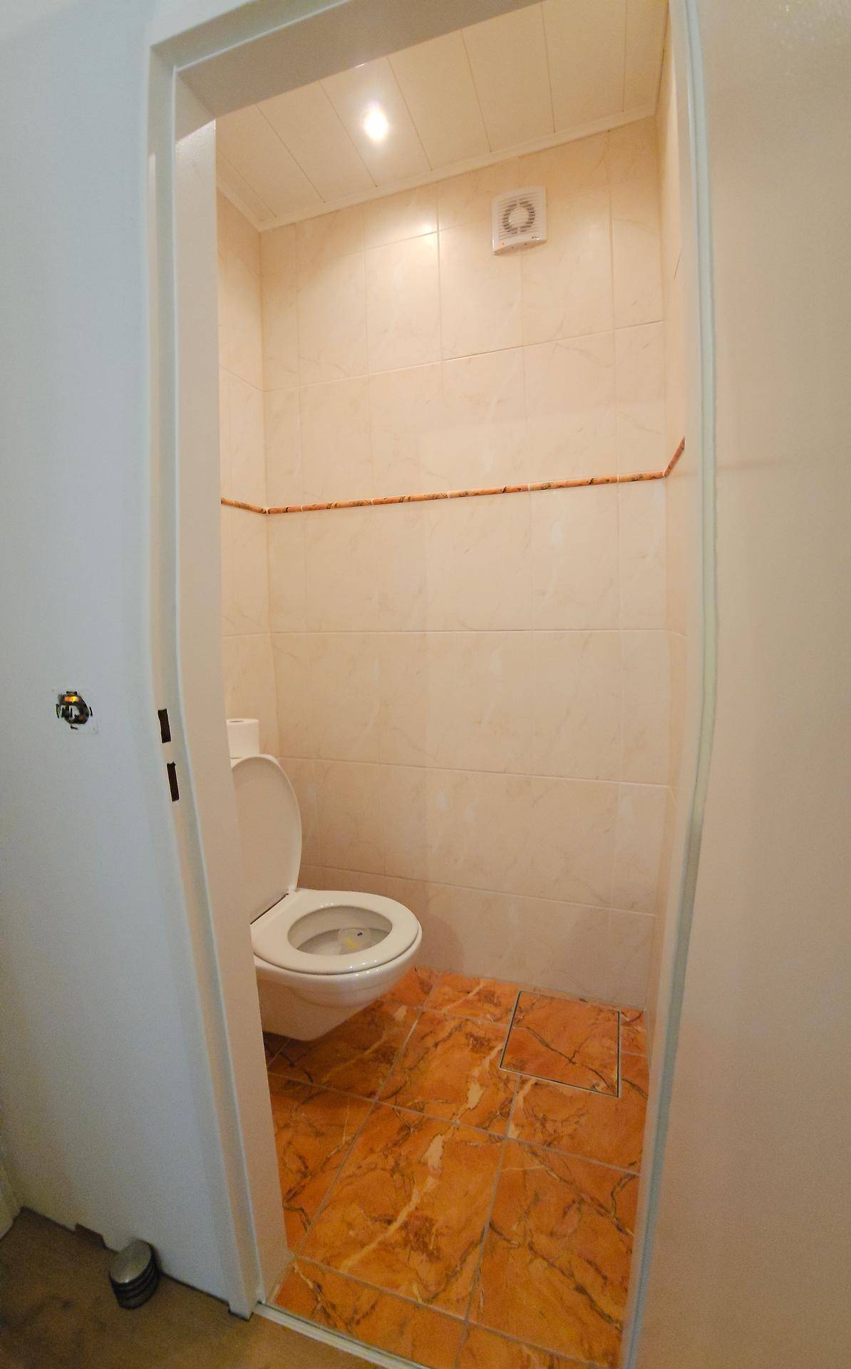Separate Toilette mit gefliesten Wänden und Terrakotta-Bodenfliesen, ausgestattet mit einem WC.