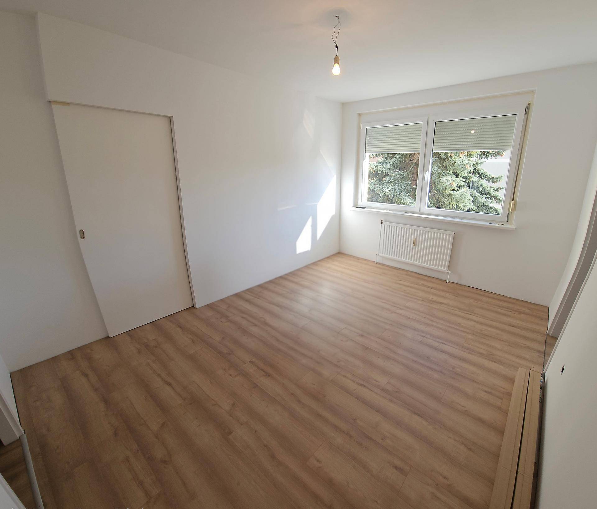 Geräumiges, helles Zimmer mit Laminatboden und Fenster mit Jalousien, ideal als Schlafzimmer.