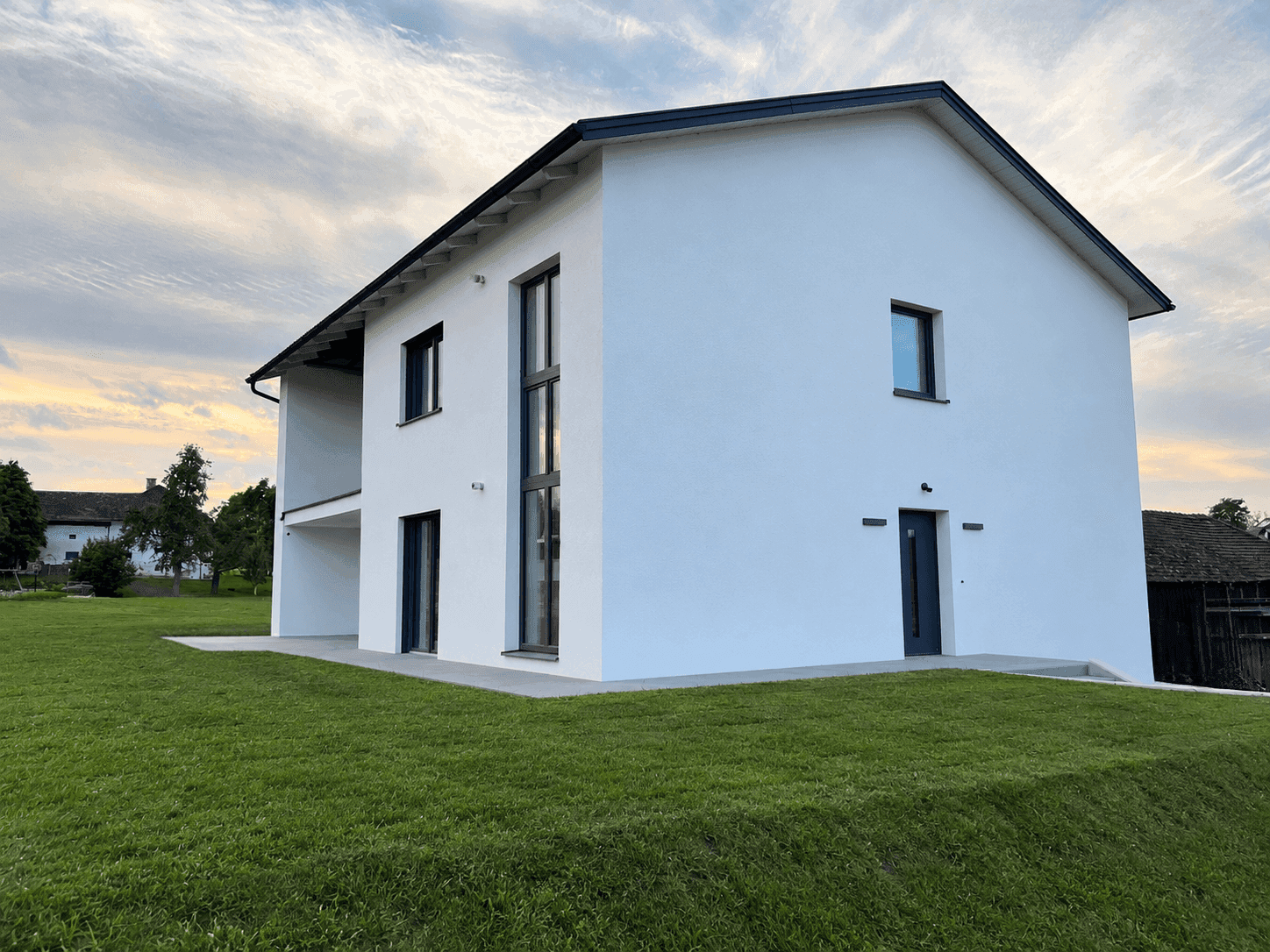Ansicht des modernen Einfamilienhauses von der Seite mit großen Fenstern und weitem Blick ins Grüne.