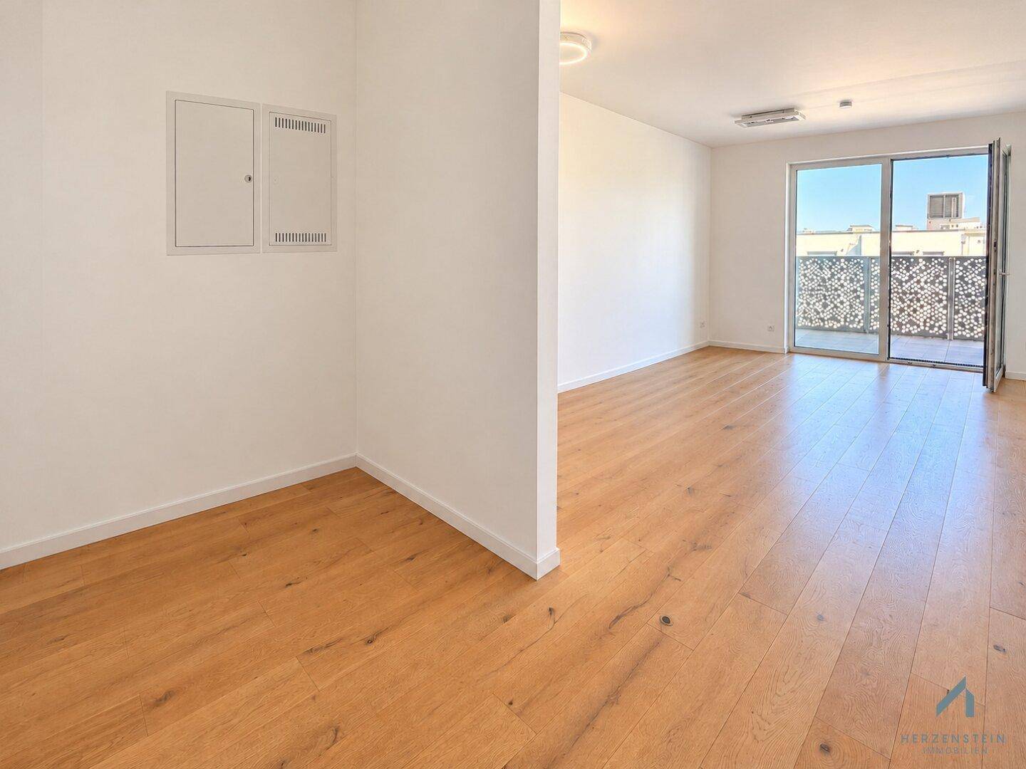 Offener Wohnbereich mit Holzparkett und Zugang zu einem Balkon, ideal für entspannte Stunden.