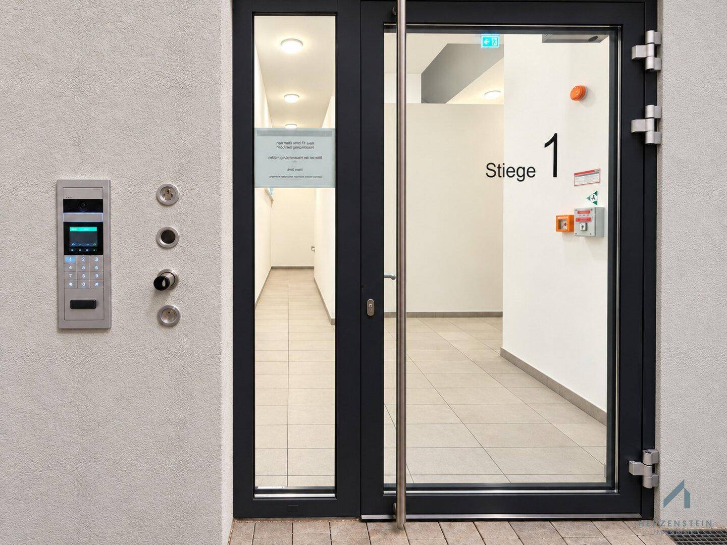 Moderner Gebäudeeingang mit Glasfront und Gegensprechanlage, der Zugang zum Treppenhaus bietet.