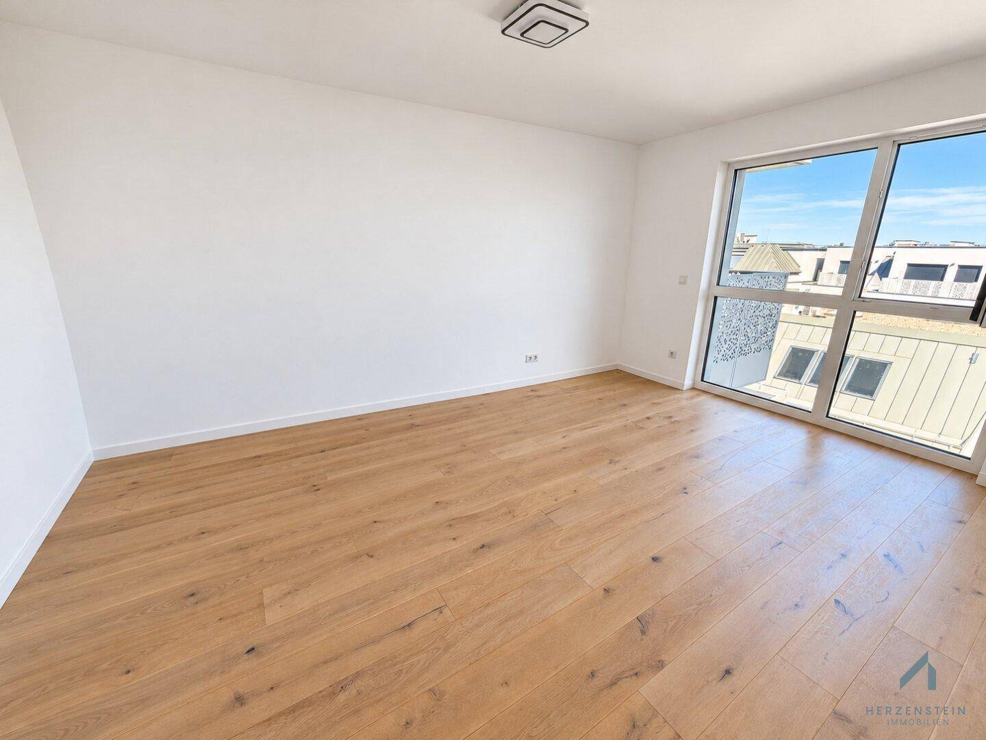 Geräumiges Zimmer mit großen Fenstern, die viel Tageslicht hereinlassen, und hellem Holzparkett.
