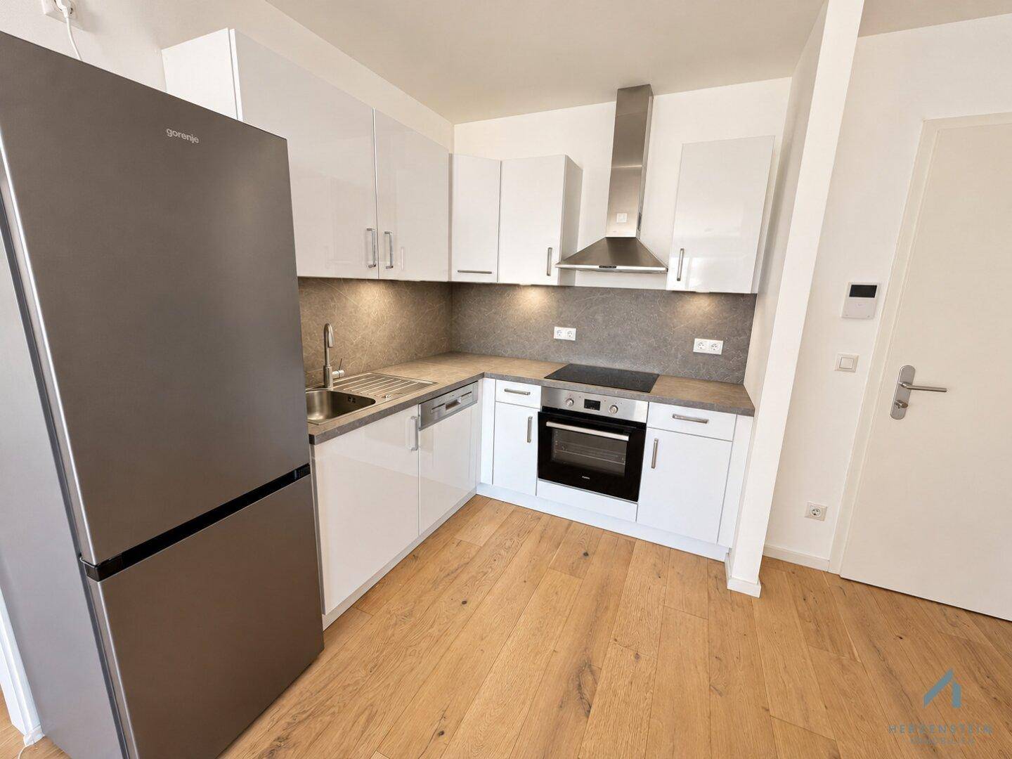Moderne Einbauküche mit weißen Hochglanzfronten, integrierten Geräten und Holzparkettboden.