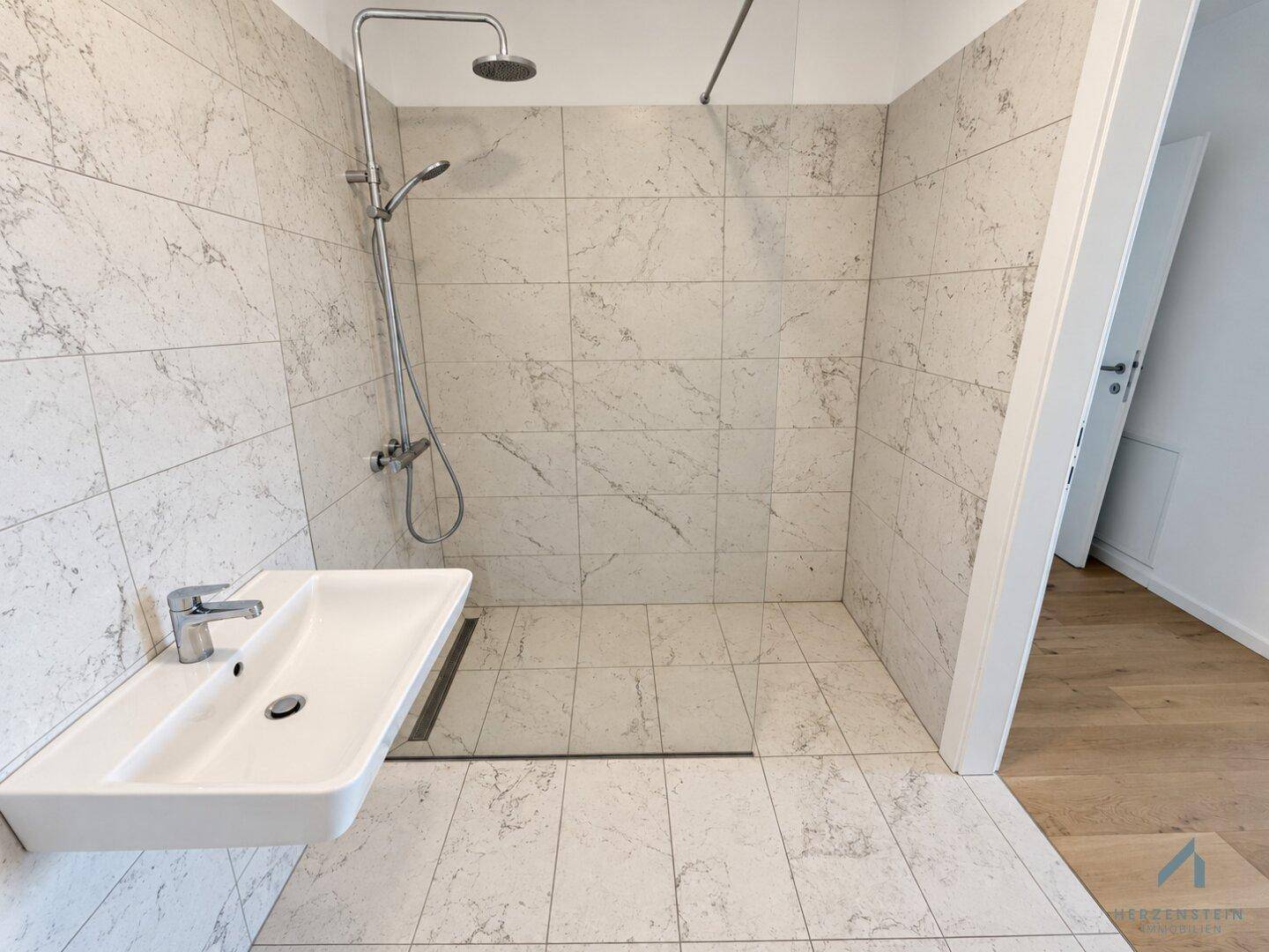 Modernes Badezimmer mit großformatigen Fliesen, ebenerdiger Dusche und minimalistischem Waschbecken.